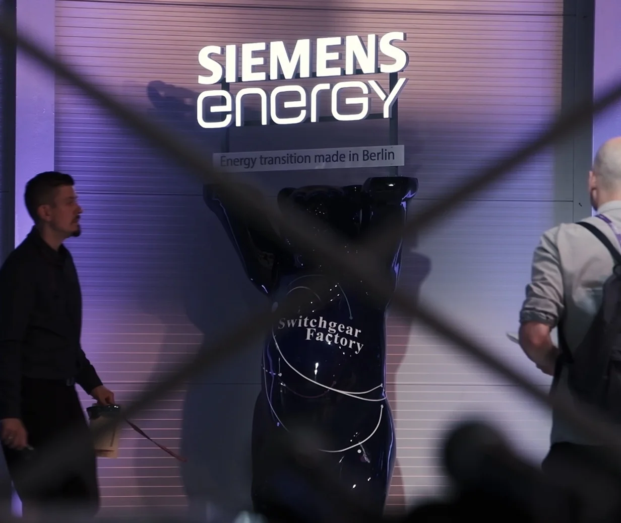 Ein Display auf einer Veranstaltung der Siemens Energie- und Schaltanlagenfabrik mit vorbeilaufenden Menschen und einem Schild mit der Aufschrift "Energiewende made in Berlin".