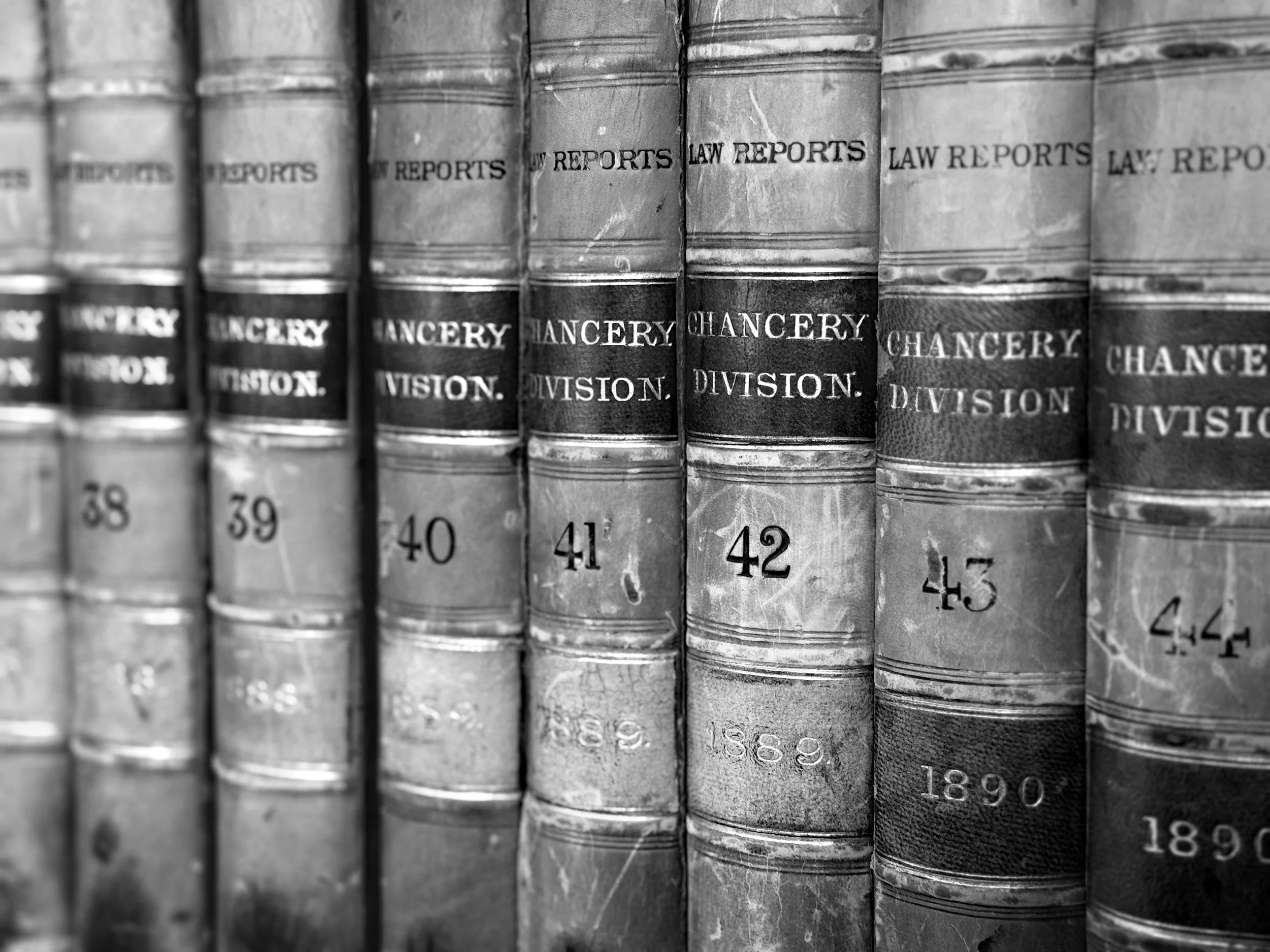 Row of old law reports books with worn, black spines and titles in gold lettering, arranged vertically on a shelf.