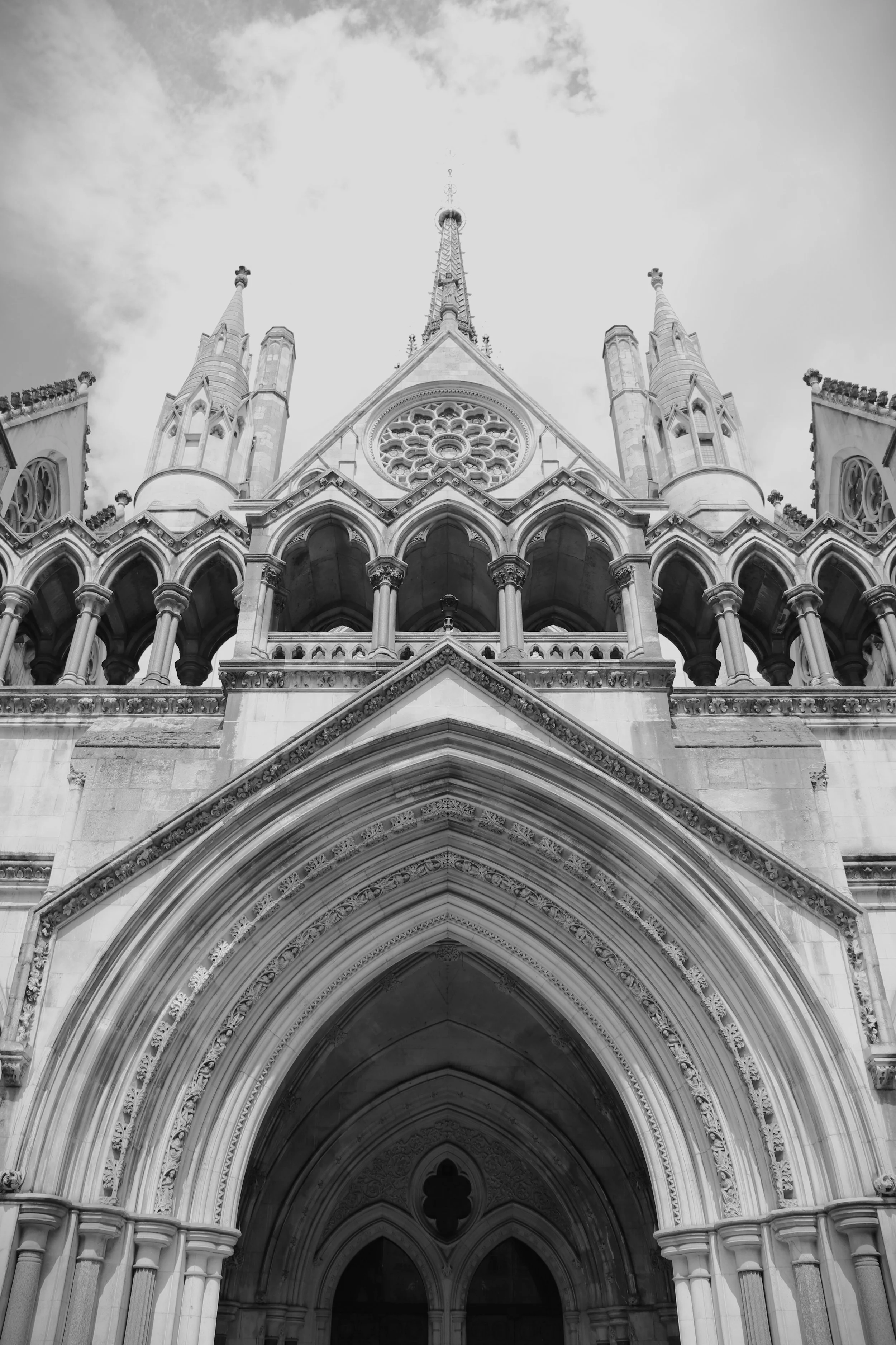 Front view of the Royal Courts of Justice with pointed arches, detailed carvings, and a large rose window, under a partly cloudy sky.