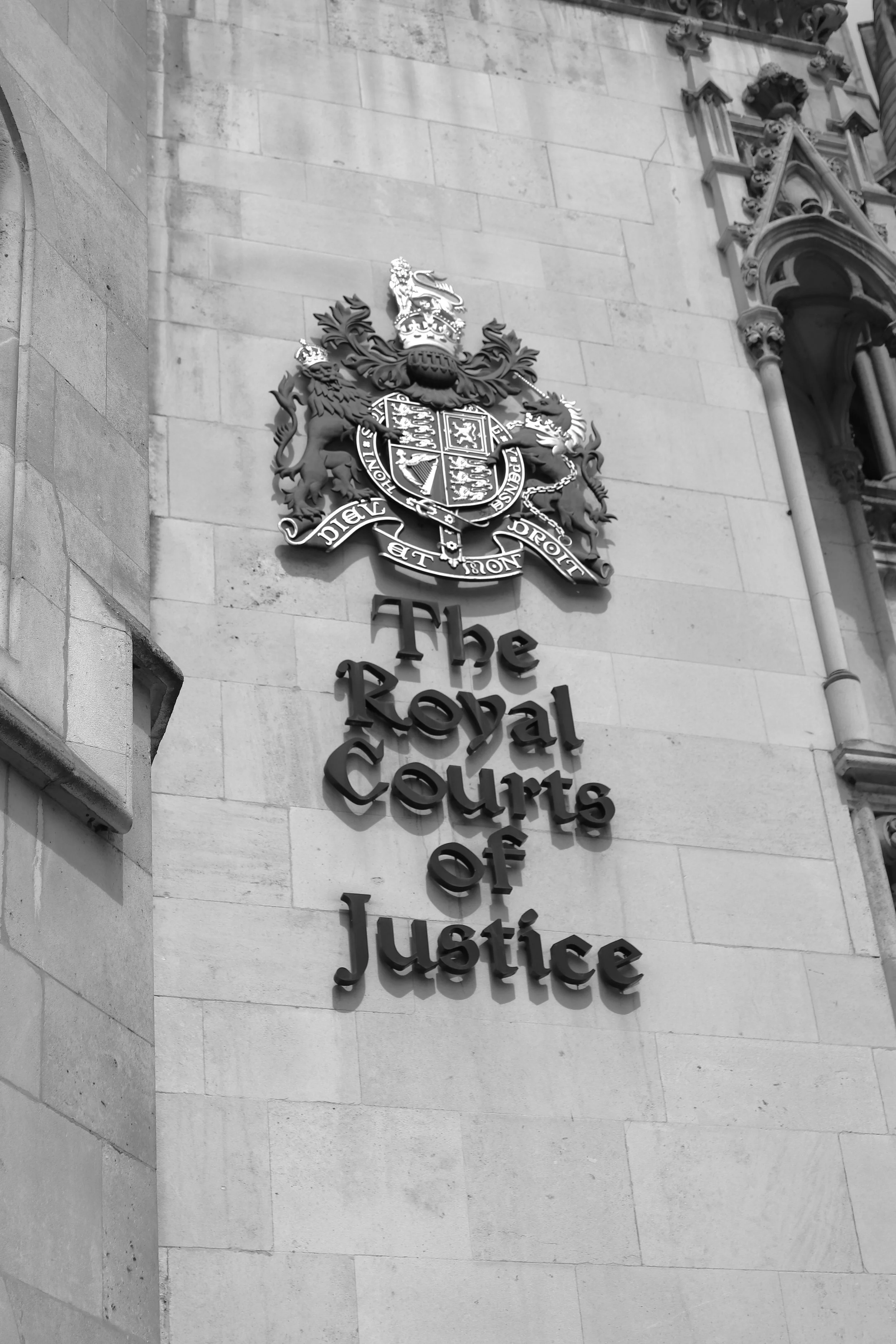 The entrance sign of the Royal Courts of Justice showing a crest with a crown and shield, and the words "The Royal Courts of Justice" on the stone wall.