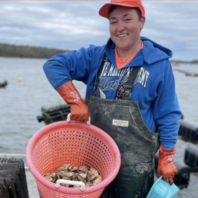 Person holding a basket of oysters near a body of water.