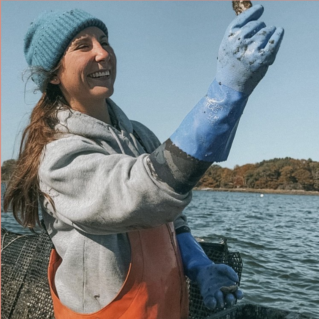 Woman in blue beanie and gloves holding a shell on a boat.