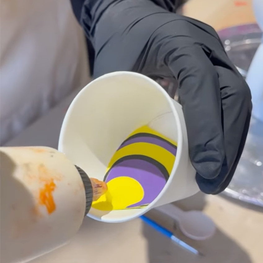 Paint is being squeezed into the side of the cup so it rolls down to the bottom resulting in paints sitting on top of each other
