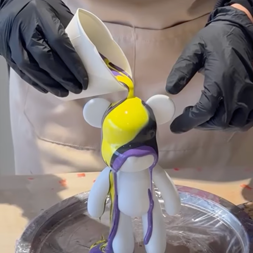 Paint being poured from a cup onto a plastic bear