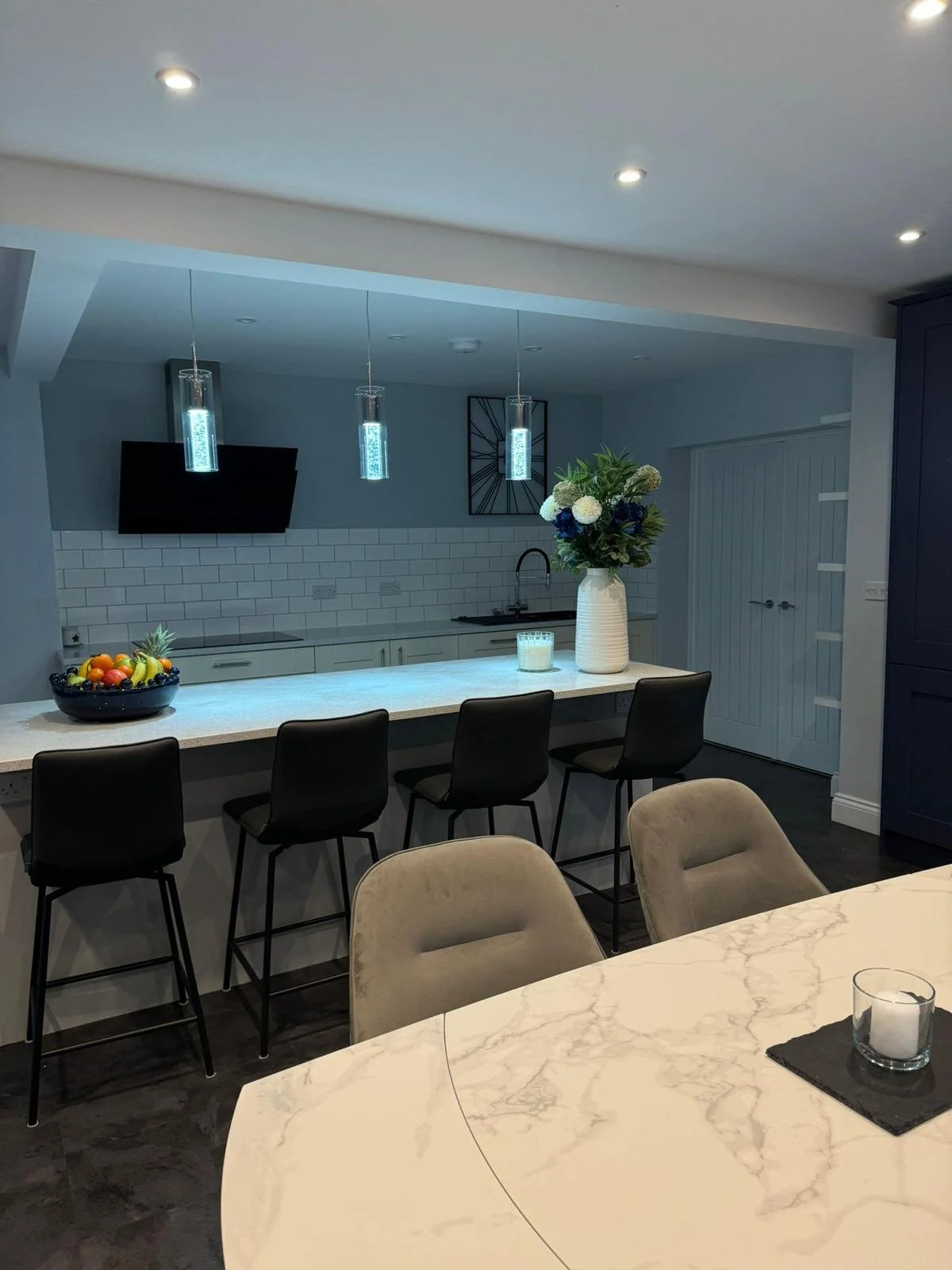 Modern kitchen with a white marble island, black stools, a vase with flowers, and pendant lighting.