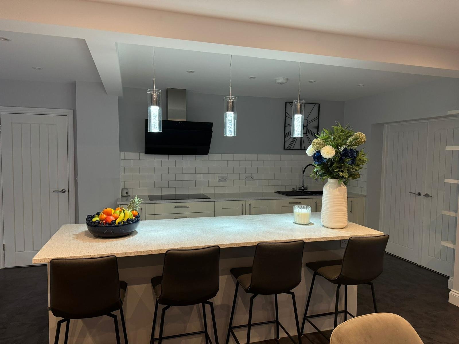 Modern kitchen with a kitchen island, fruit bowl, large vase with flowers, and three pendant lights overhead.