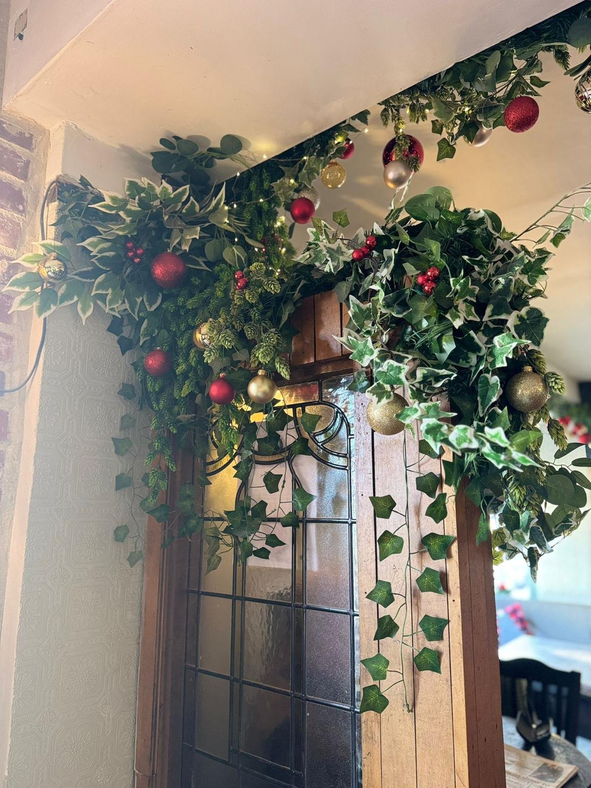 Decorative Christmas garland with red, gold, and silver ornaments and green foliage hanging above a doorway with a glass-paneled door.