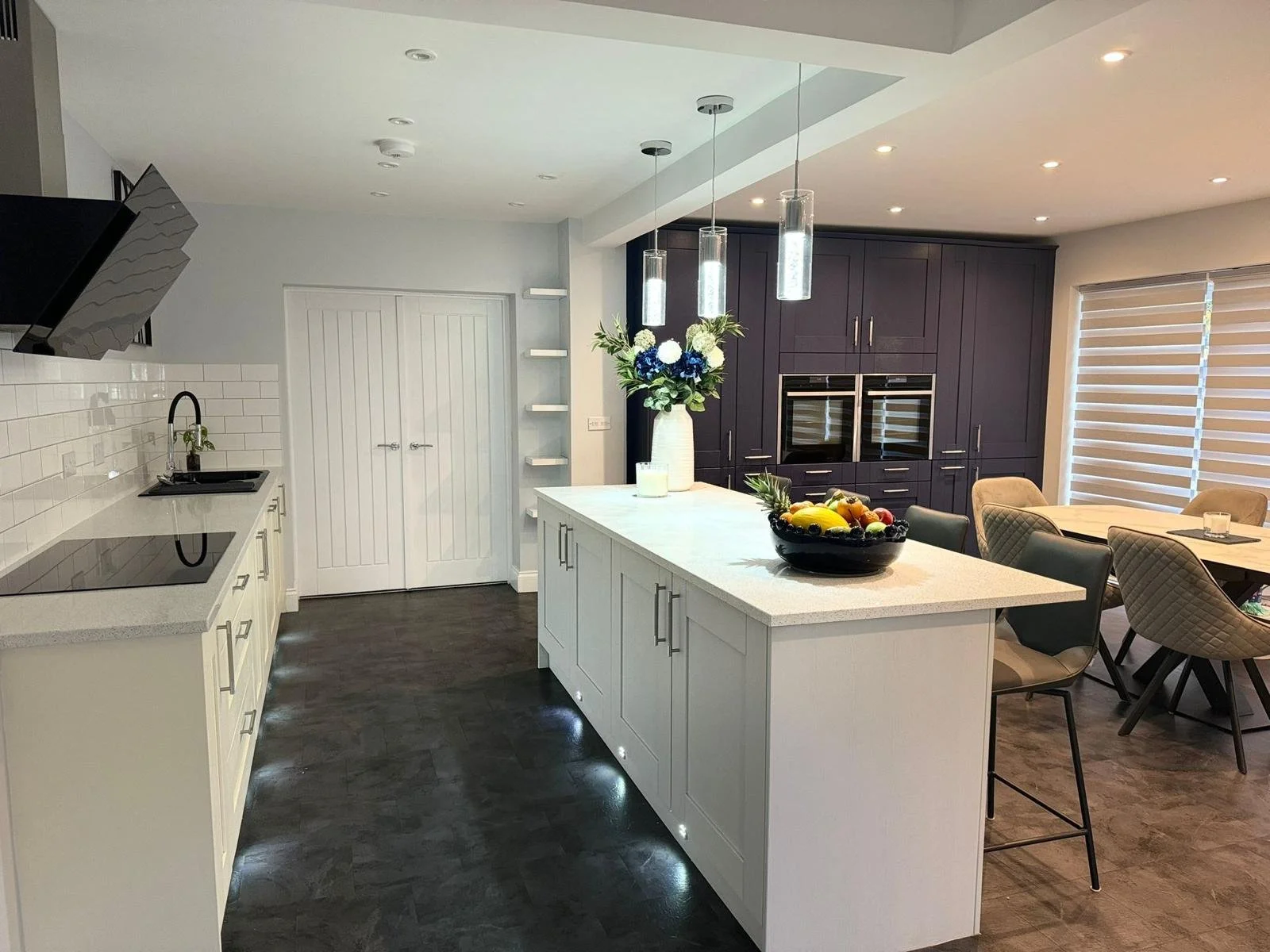 Modern kitchen with white island, dark cabinetry, and dining area with chairs.