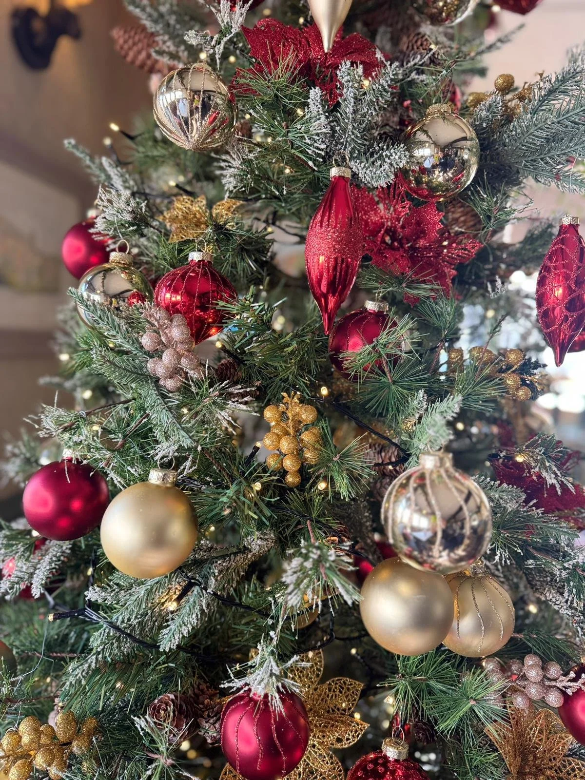 Decorated Christmas tree with red, gold, and silver ornaments, gold berries, glittering leaves, and white lights.