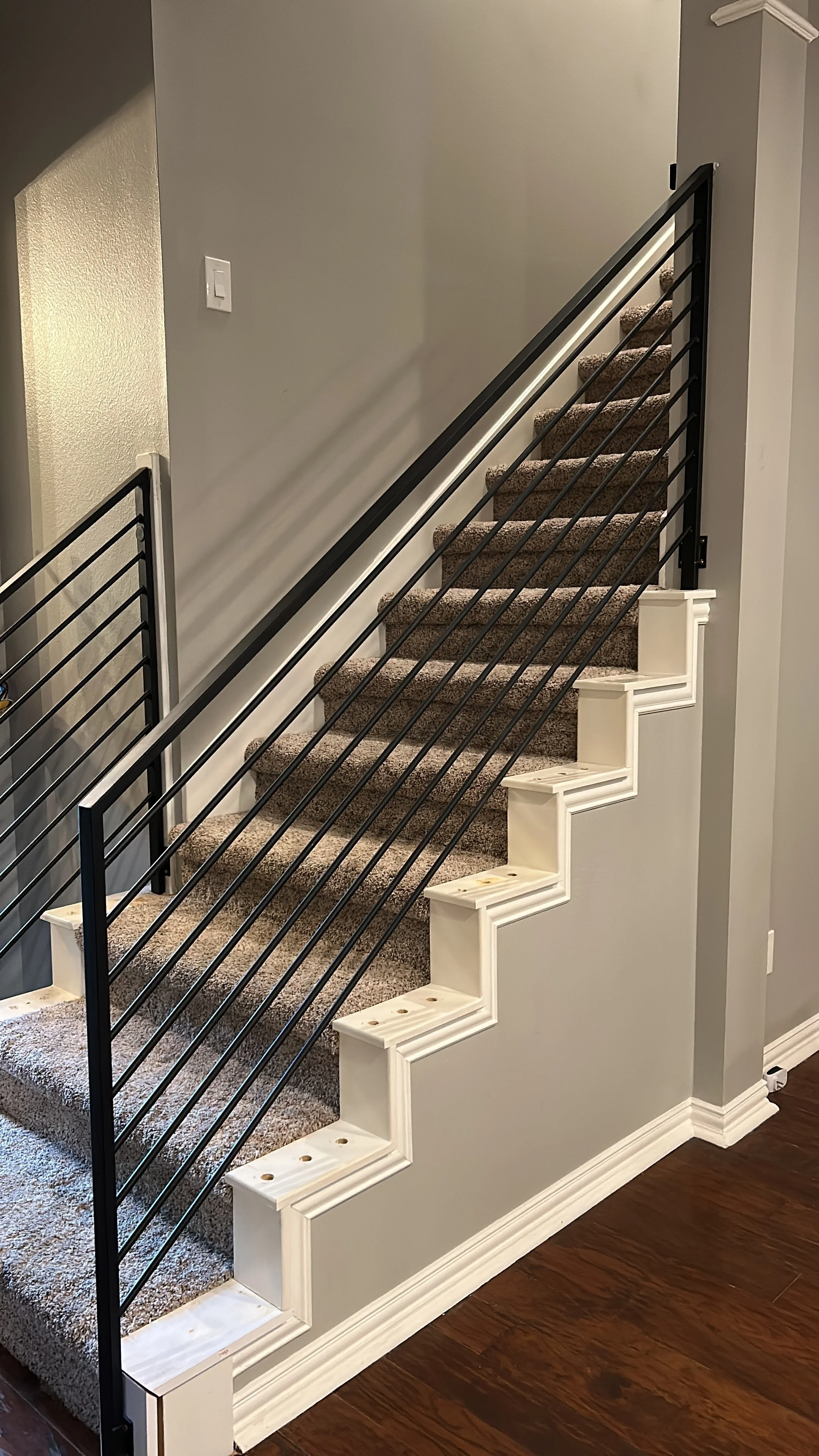 A staircase under construction with carpeted steps, black metal railings, and white wooden trim, in an indoor residential setting.