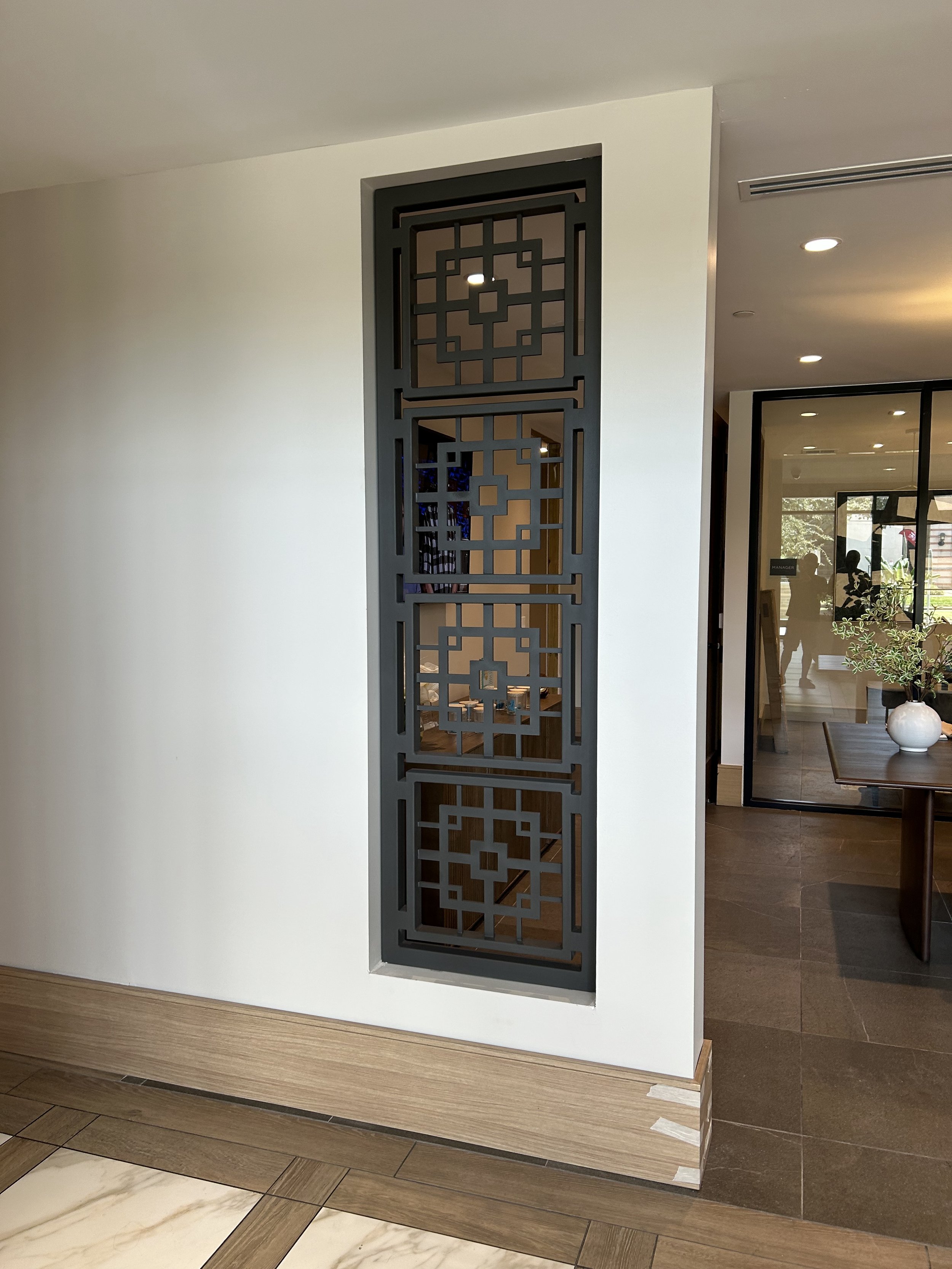 Decorative black metal screen with geometric patterns on a white wall in an interior space.