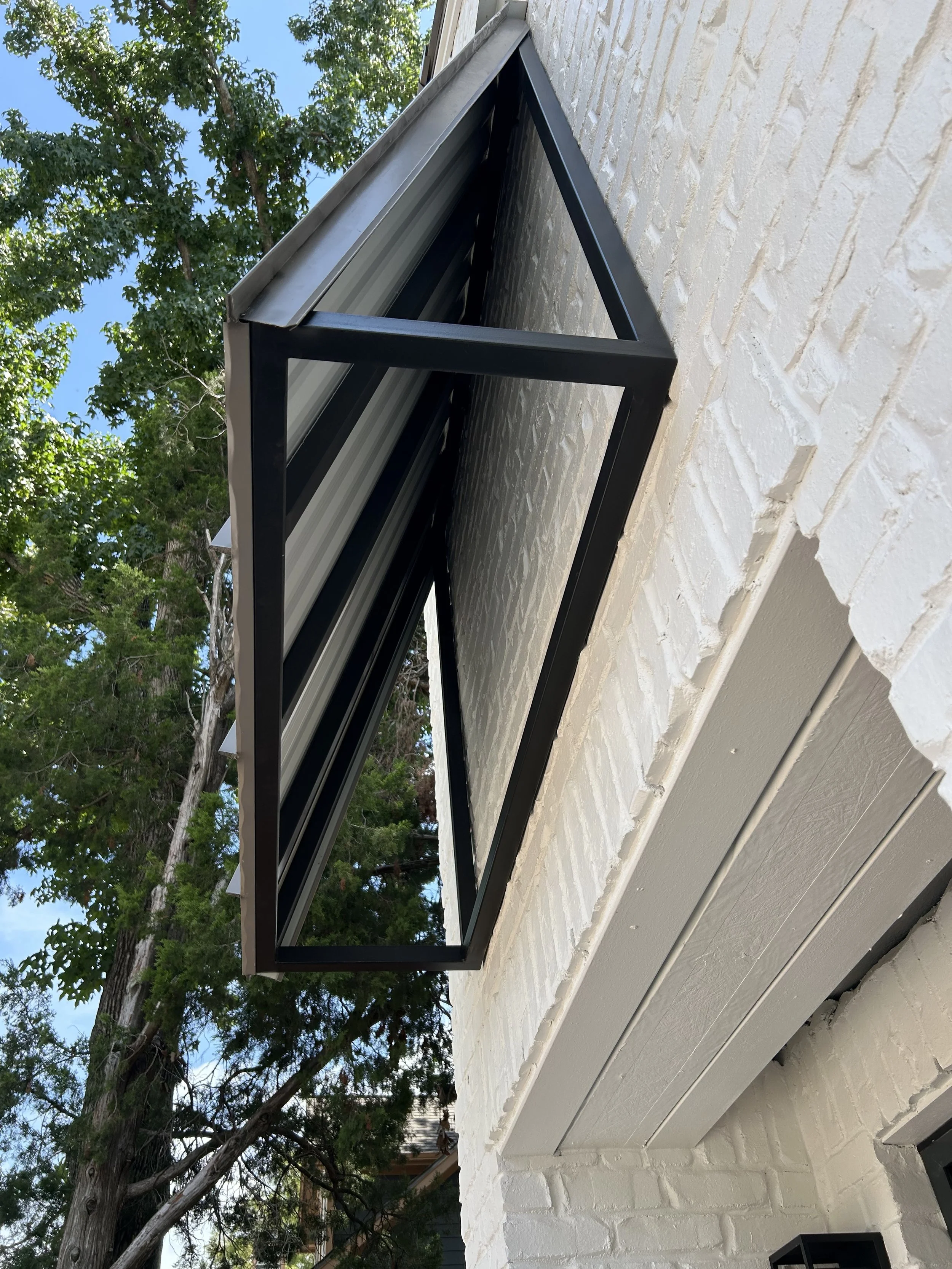 Black metal window frame with curved glass installed on a white painted brick wall of a building.