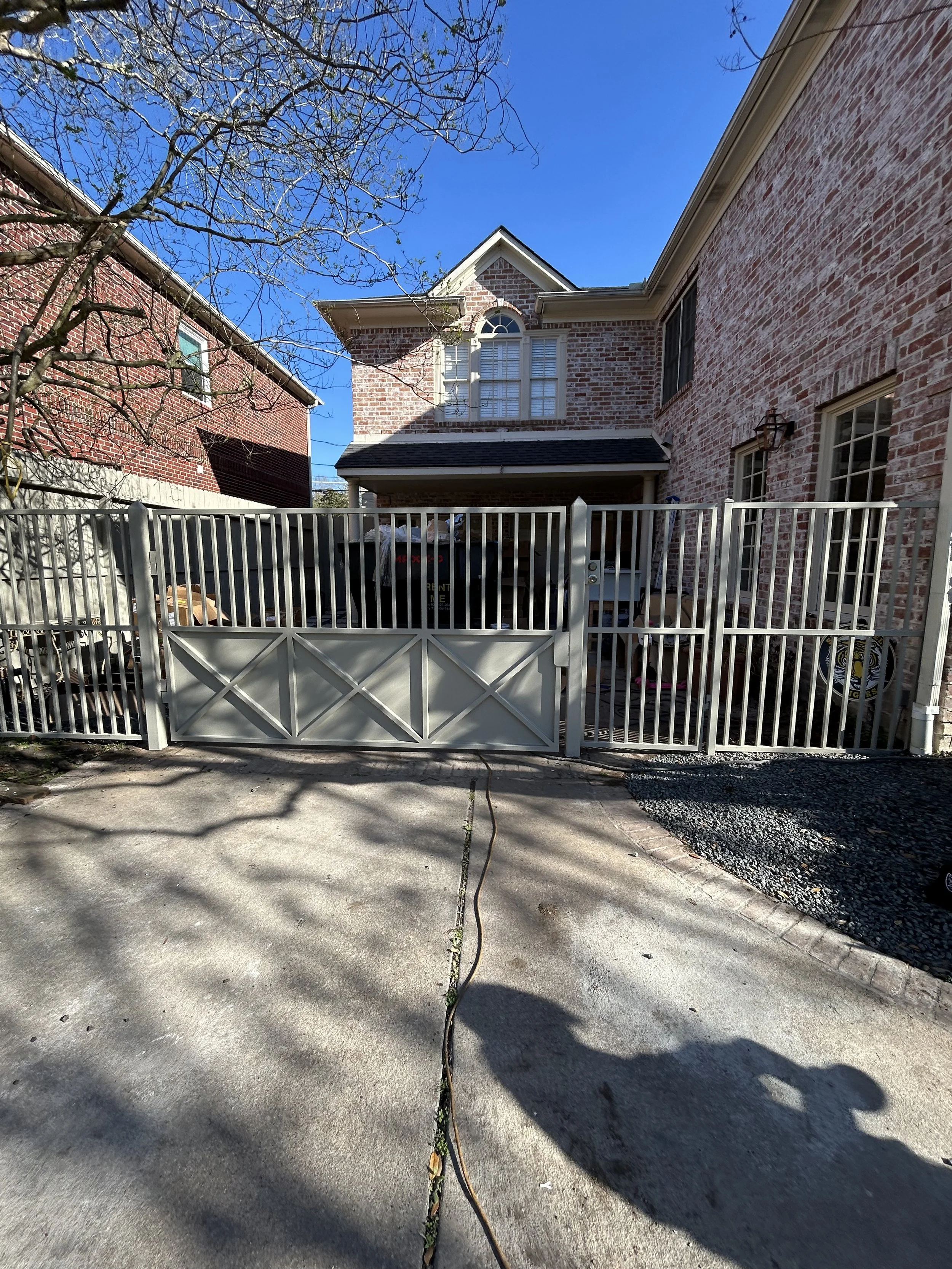 View of a brick house with a gated backyard, a tree with no leaves, and clear blue sky.
