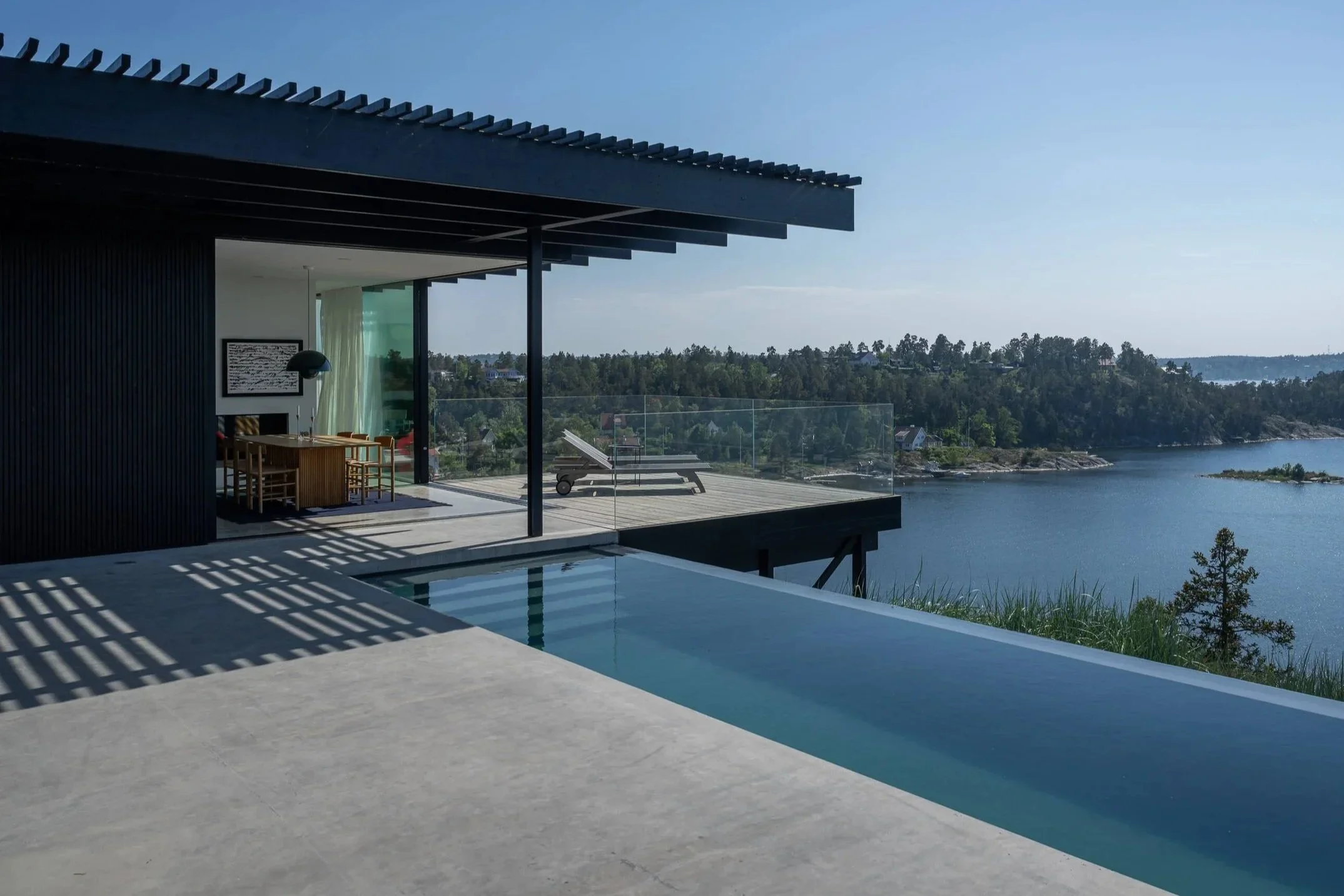 Modernes Haus mit Infinity-Pool, Terrasse und Blick über einen See mit Bäumen.