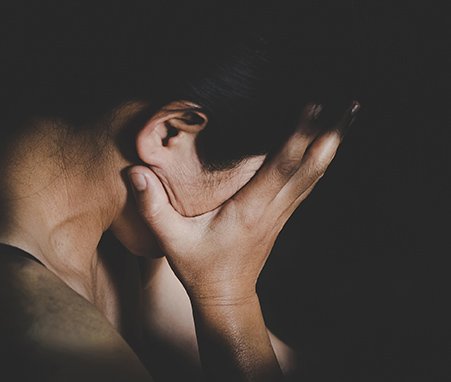 women with dark hair obscuring her face with her hands in distress against in shadowy lighting