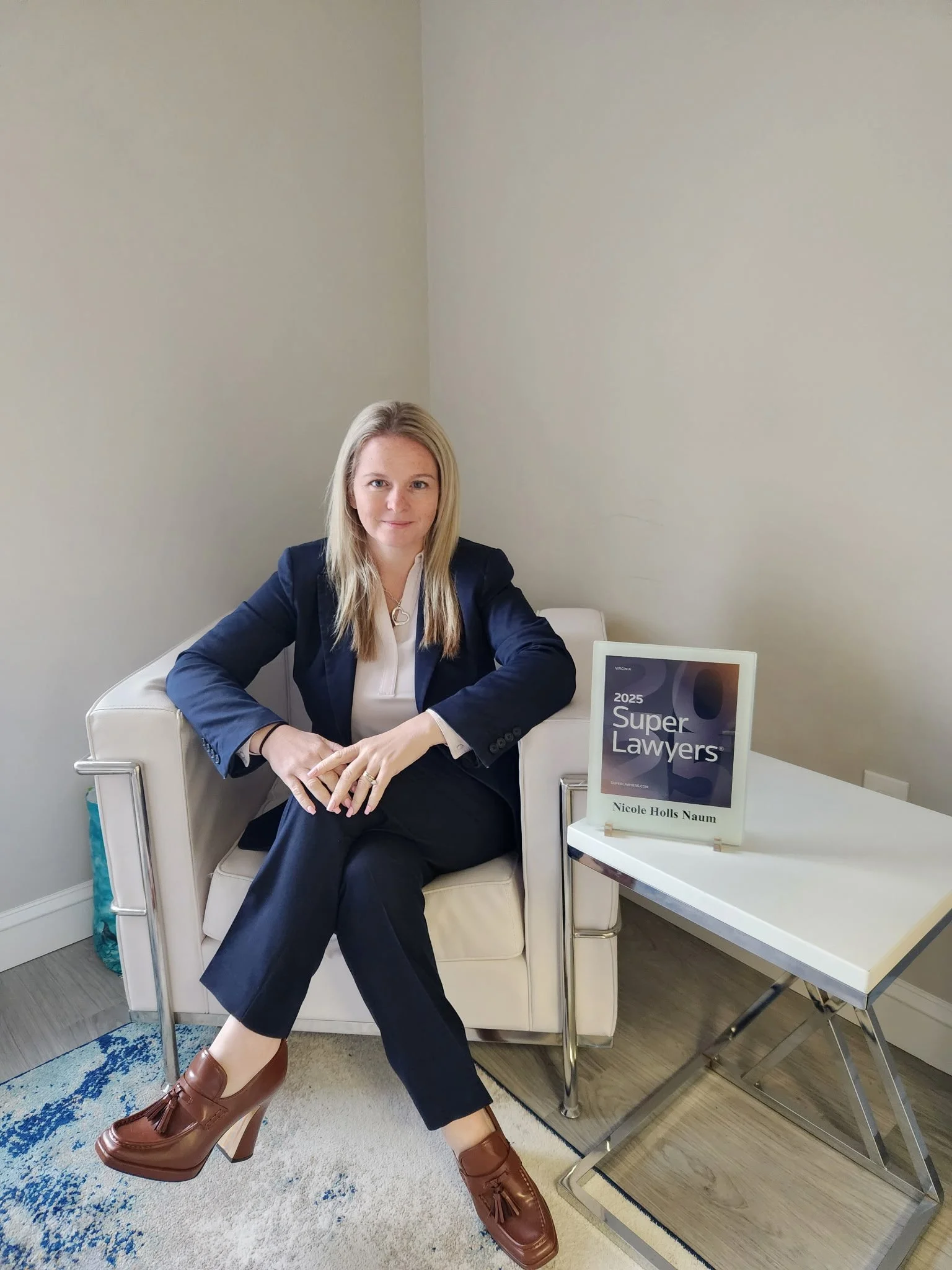 confident blonde attorney in a suit sitting with her legs crossed, next to her award as a Super Lawyer