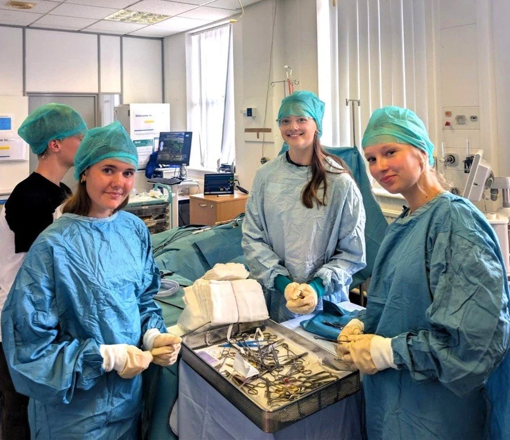 Four teenagers on a Medical work experience in surgical scrubs and caps standing around a surgical tray with medical tools in an operating room.