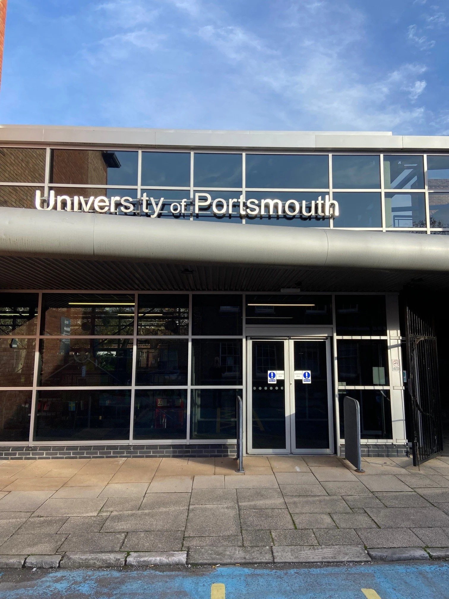 Entrance to the University of Portsmouth building with large windows and a sign on top.