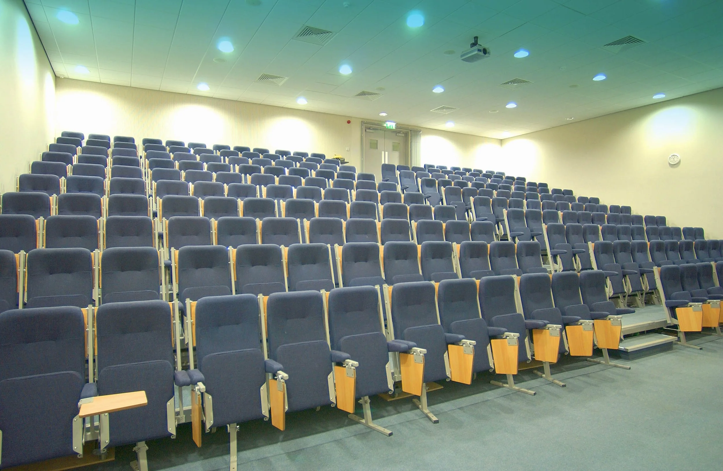 Empty lecture hall at the university of surrey with tiered rows of dark blue seats and small wooden armrests.