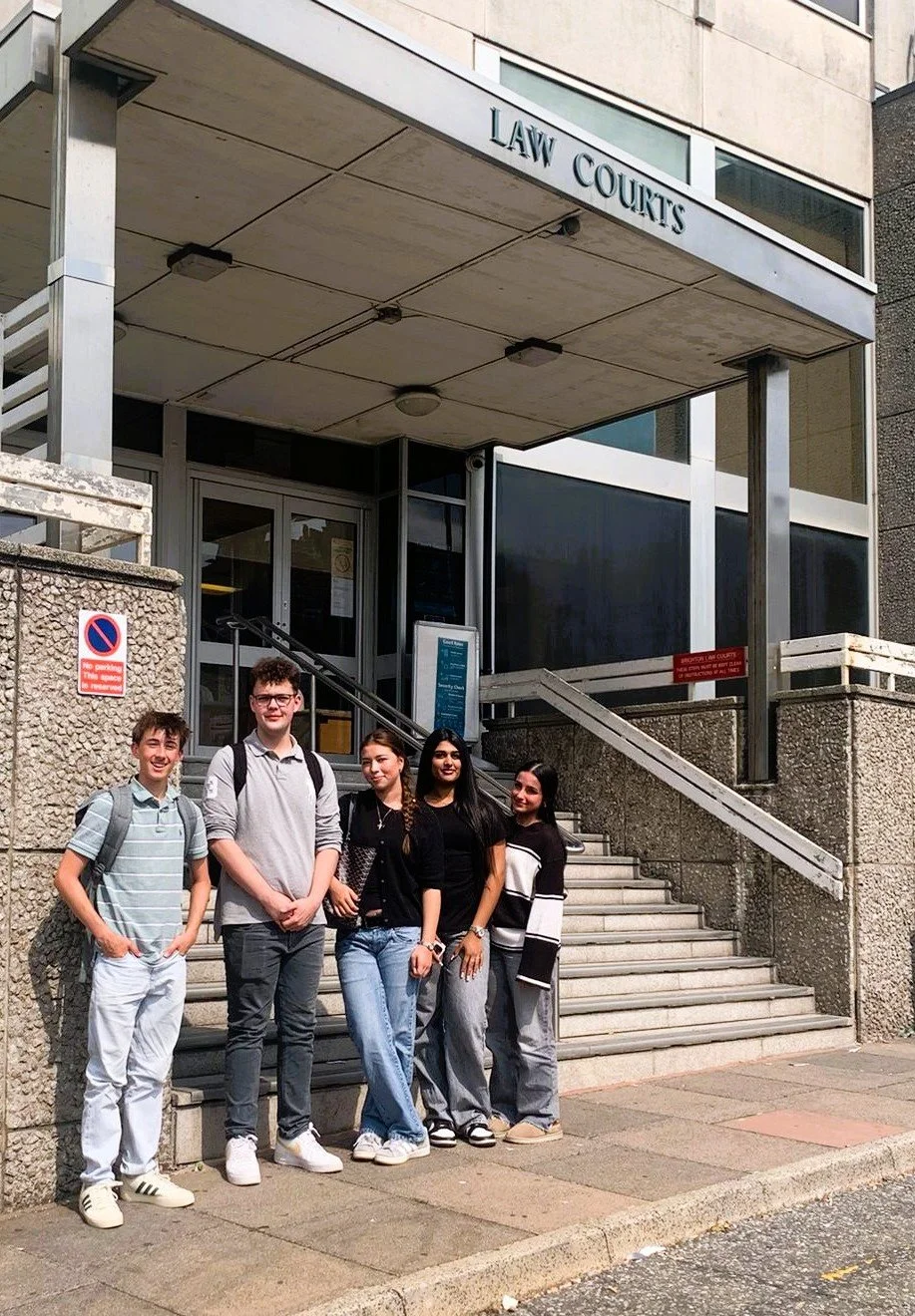 A group of five teenagers standing outside the entrance to a law courts building, with stairs leading up to the entrance and a sign that reads 'Law Courts'.