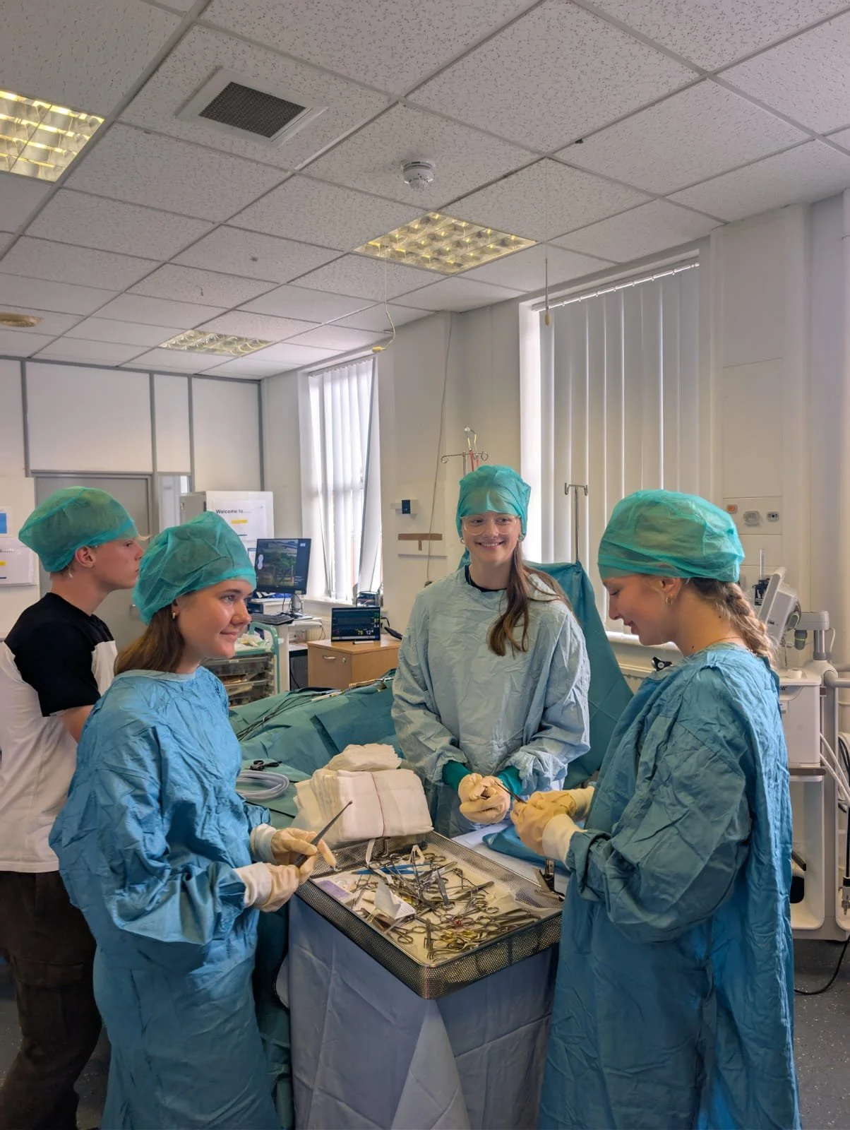 Group of five young medical professionals in scrubs and surgical caps in an operating room, gathered around a tray of surgical instruments, preparing for a procedure.