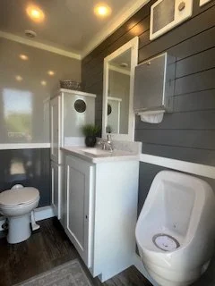 spacious luxury restroom trailer interior featuring a sink vanity, mirror, flushing toilet, urinal, and climate-controlled comfort