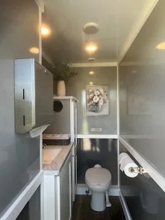 bright and spacious luxury restroom trailer interior with a flushing toilet, running water sink, premium lighting and upscale finishes