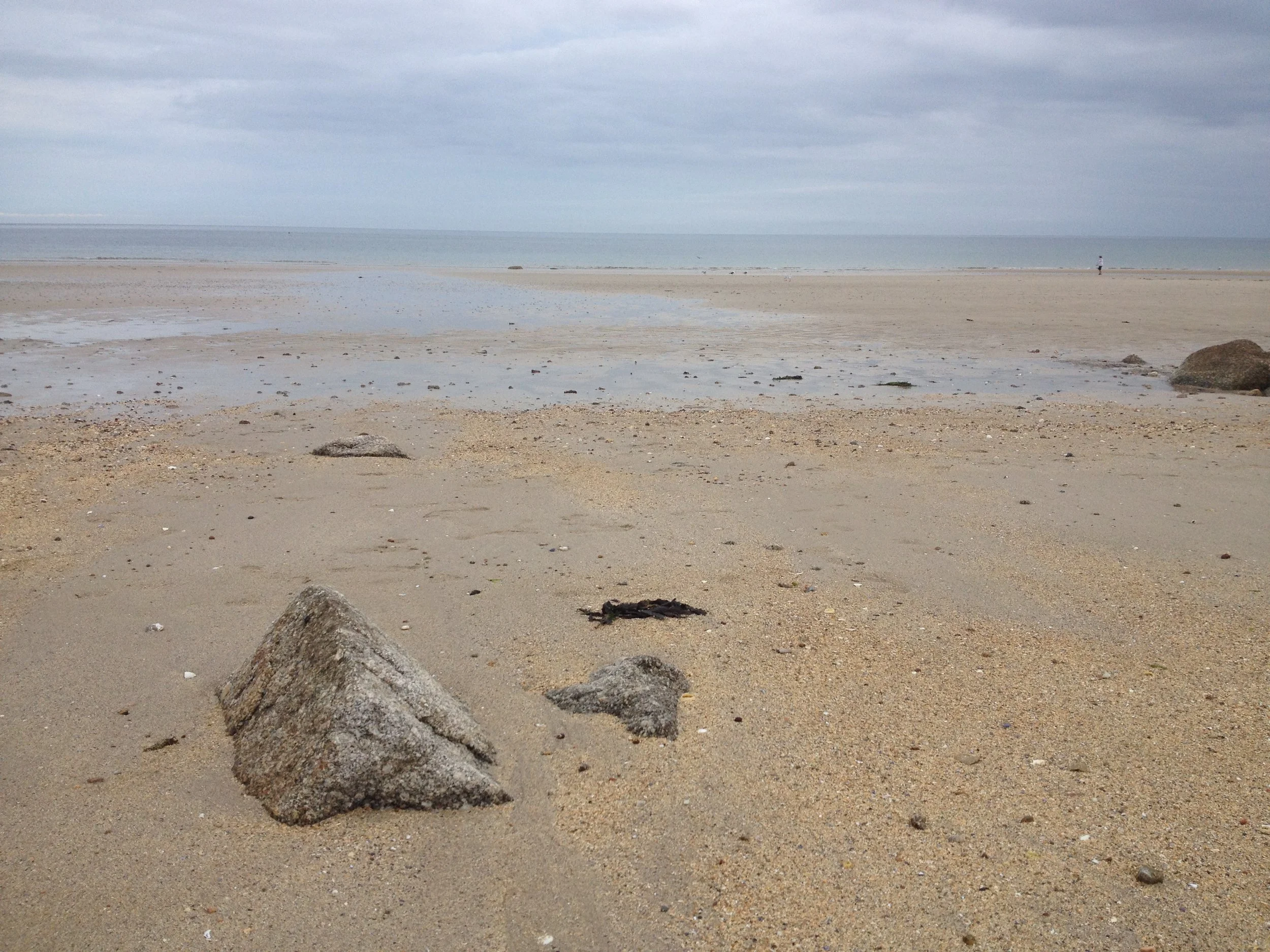 Une plage avec du sable, quelques rochers, et la mer à l'horizon sous un ciel nuageux.
