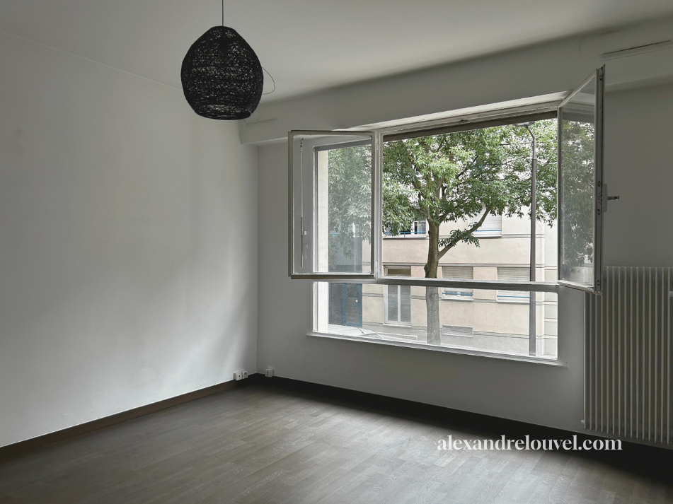 Intérieur d'une pièce vide avec un grand fenêtre ouverte donnant sur un arbre en dehors.