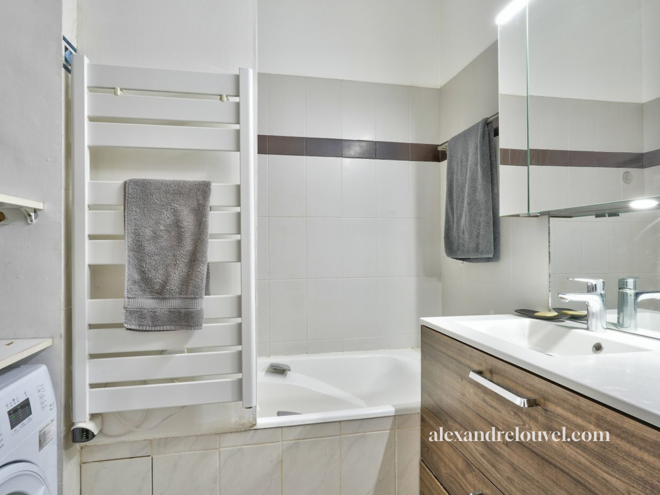 Salle de bain avec lavabo, miroir, serviettes grises, baignoire, et sèche-linge