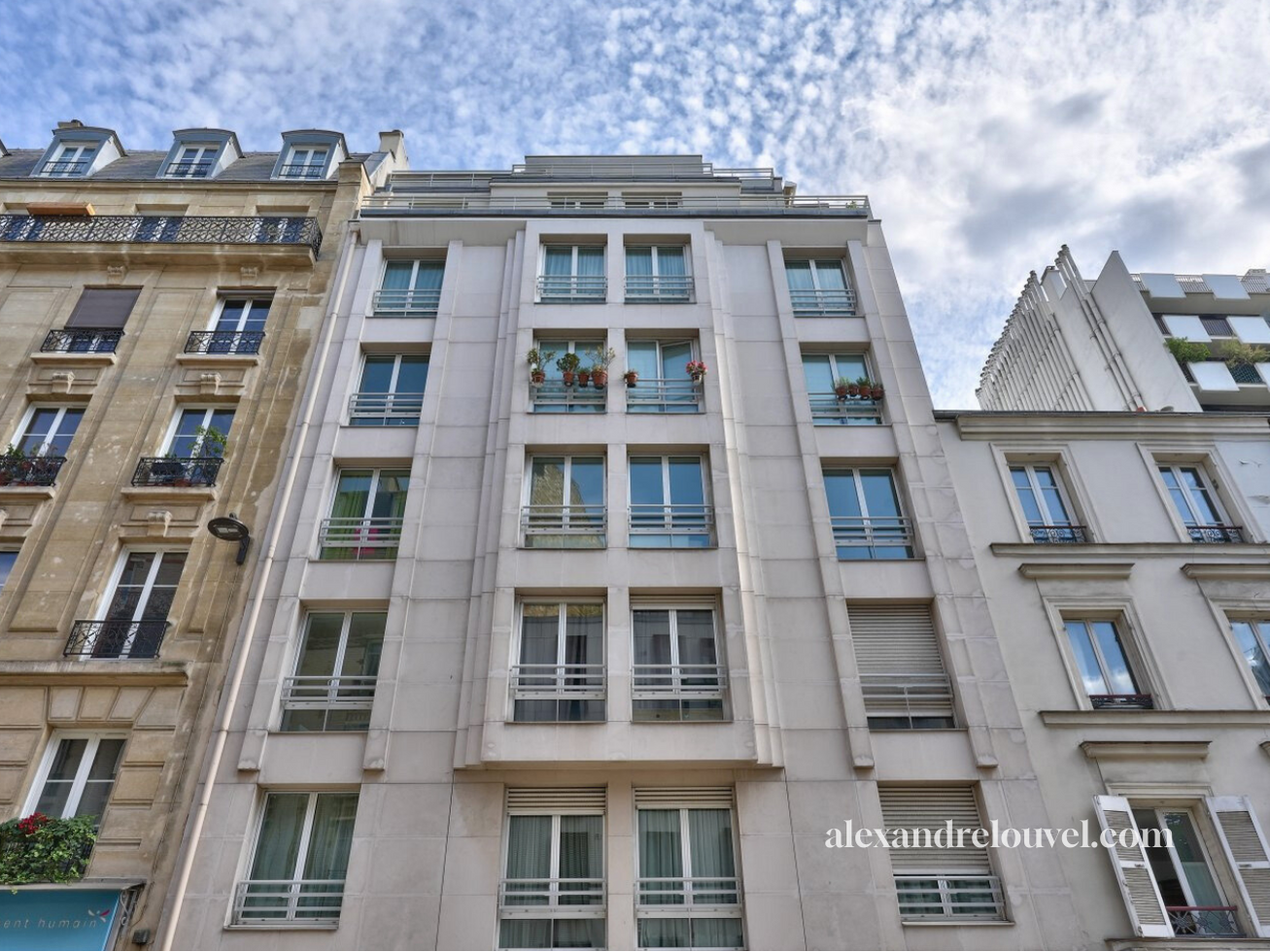 Façade d'un immeuble résidentiel moderne avec plusieurs fenêtres et balcons, sous un ciel partiellement nuageux.