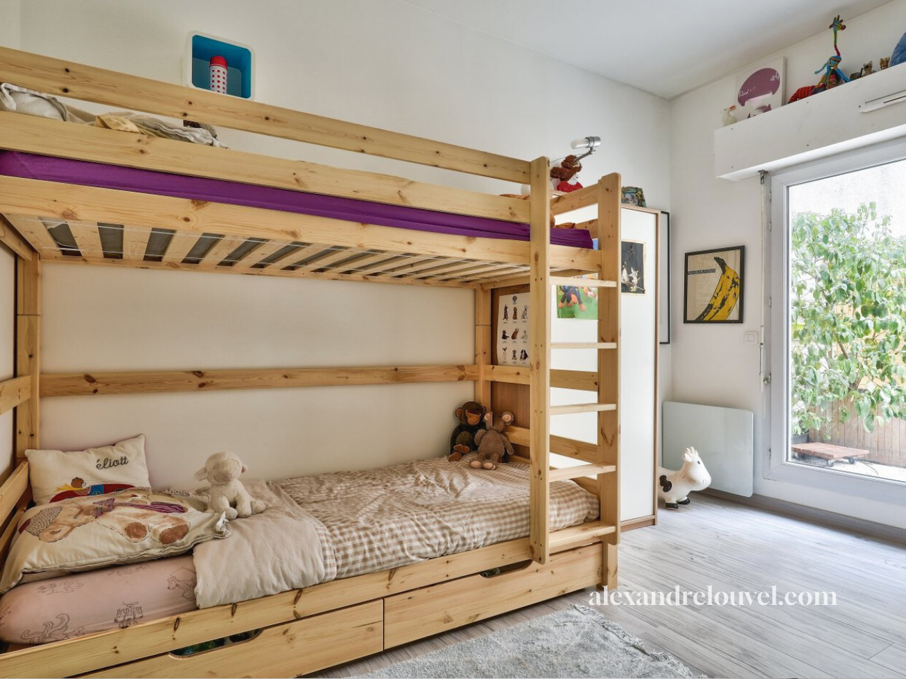 Chambre d'enfant avec un lit superposé en bois, jouets et décorations, fenêtre donnant sur un jardin, par rapport à un style moderne et lumineux.