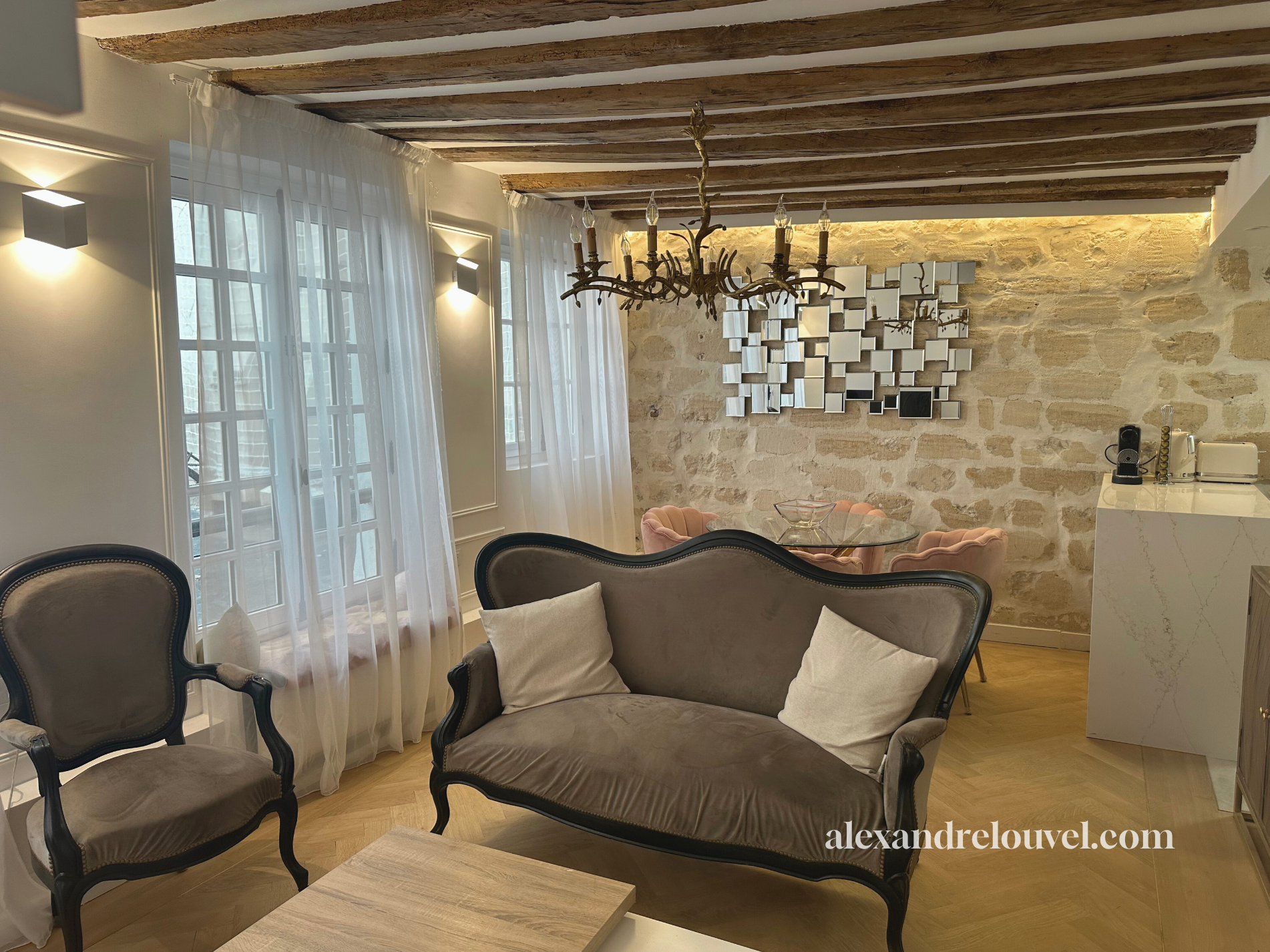 Salon avec mobilier vintage, murs en pierre, lustre en bois et miroir géométrique