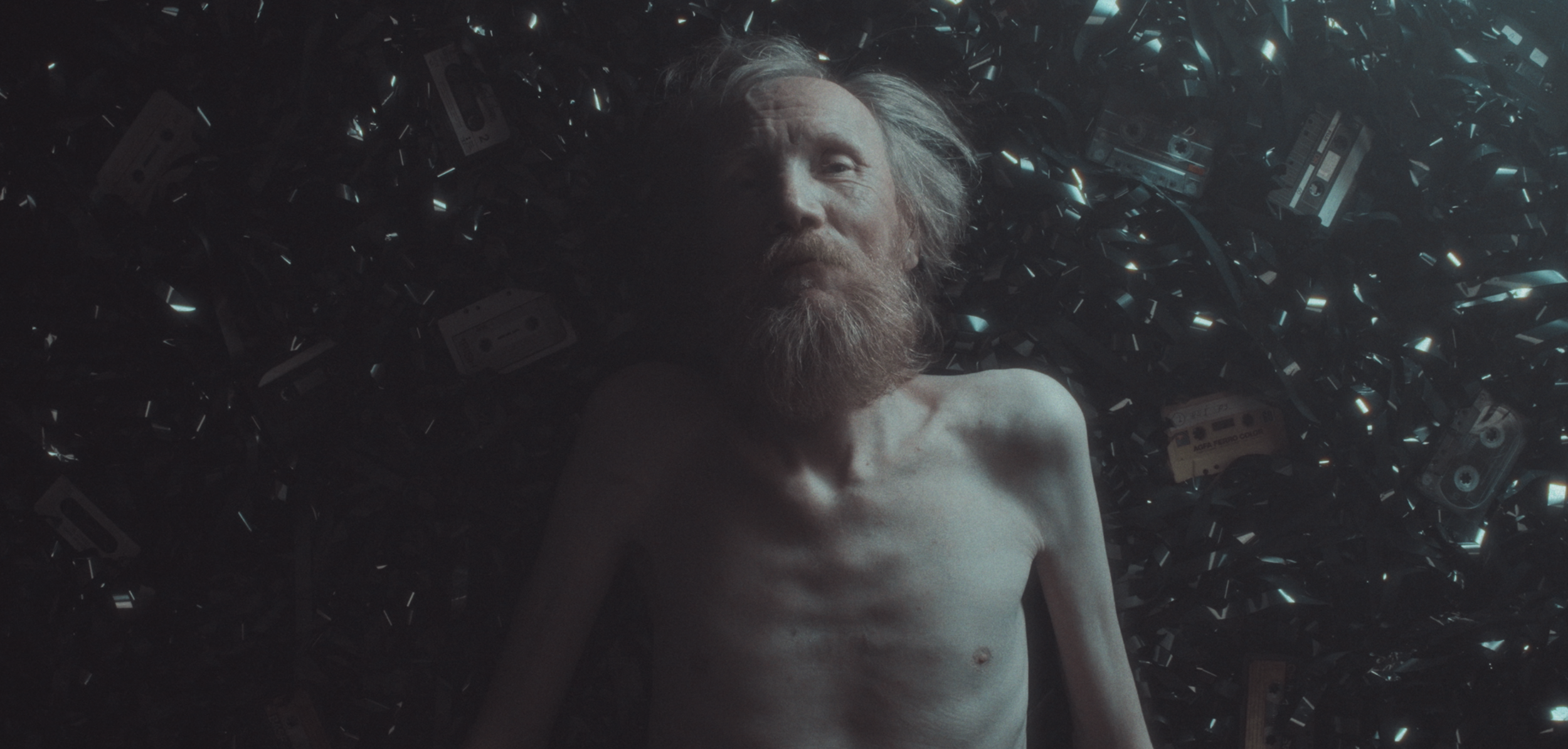 En rødhåret mand med skæg ligger på ryggen, omgivet af mange gamle kasettebånd | Dokumentarfilm | Retrograd | Esben Persson & Anders Mielcke | Filmproduktion Aarhus | GESTALT