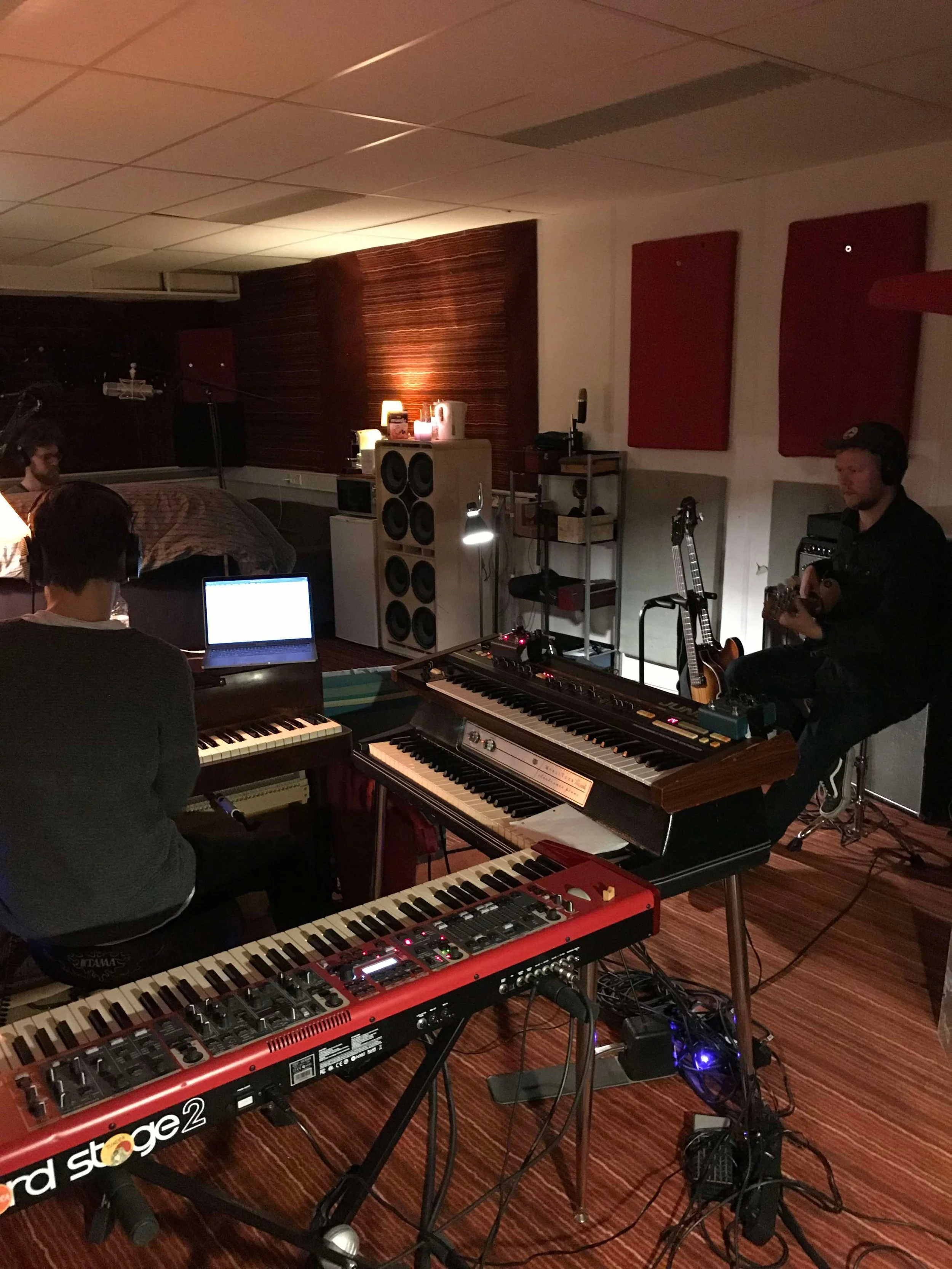 Indendørs musikstudie med en person, der spiller på et keyboard, og en anden person, der spiller guitar, omgivet af musikudstyr | Studieproduktion | Musikkomposition | Filmproduktion Aarhus | GESTALT