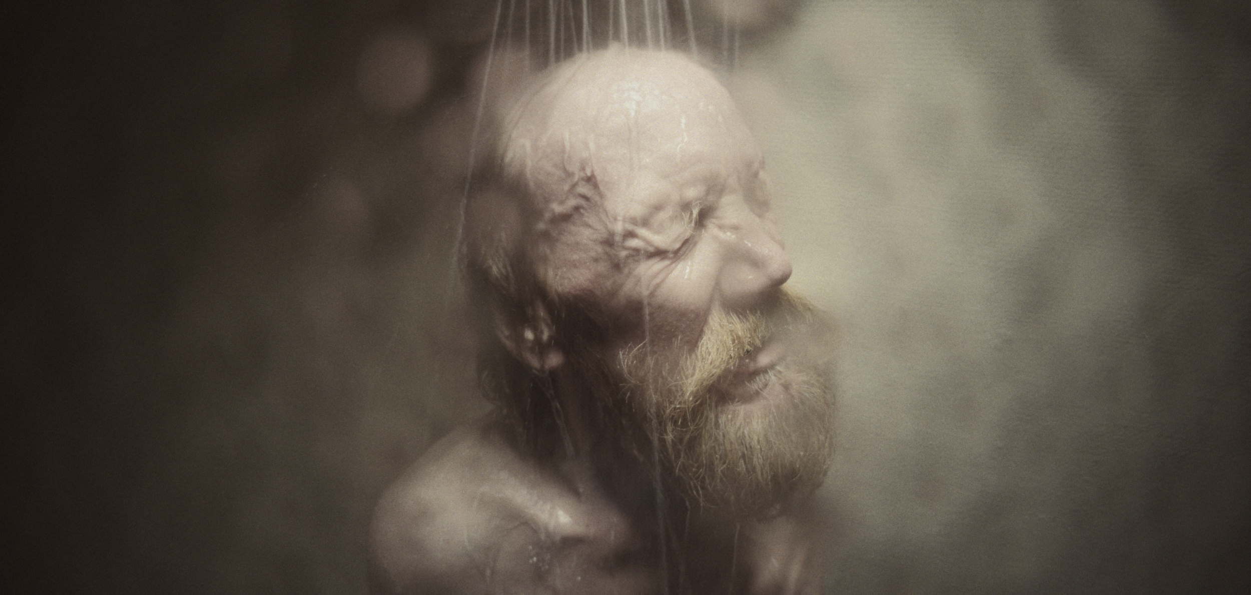 Et menneske med lukkede øjne under brusebad, mens vand strømmer ned ad ansigtet | Dokumentarfilm | Retrograd | Esben Persson & Anders Mielcke | Filmproduktion Aarhus | GESTALT