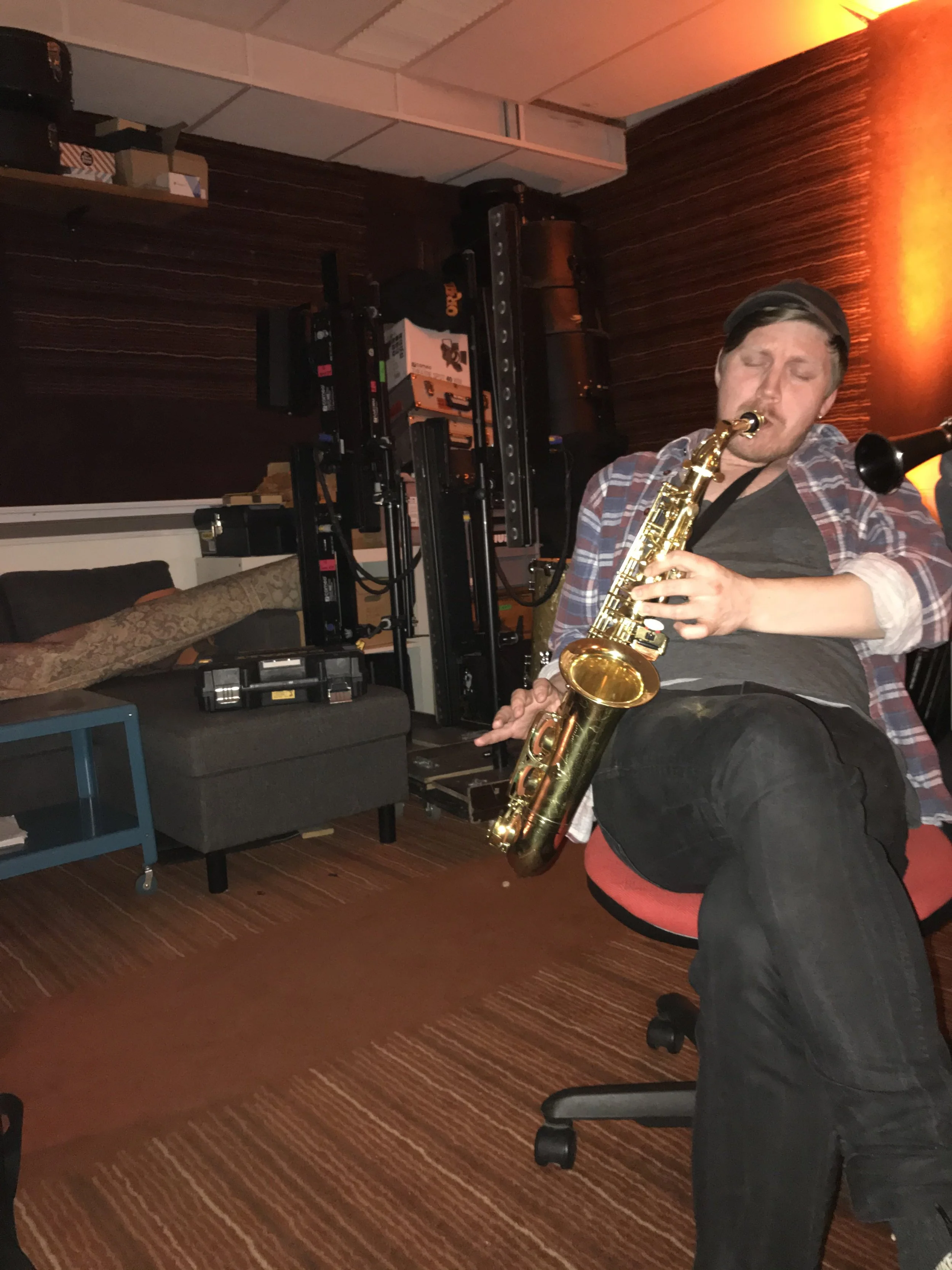 En person spiller saxofon i et musiklokale med musikudstyr i baggrunden | Musikkomposition | Lyddesign | Filmproduktion Aarhus | GESTALT