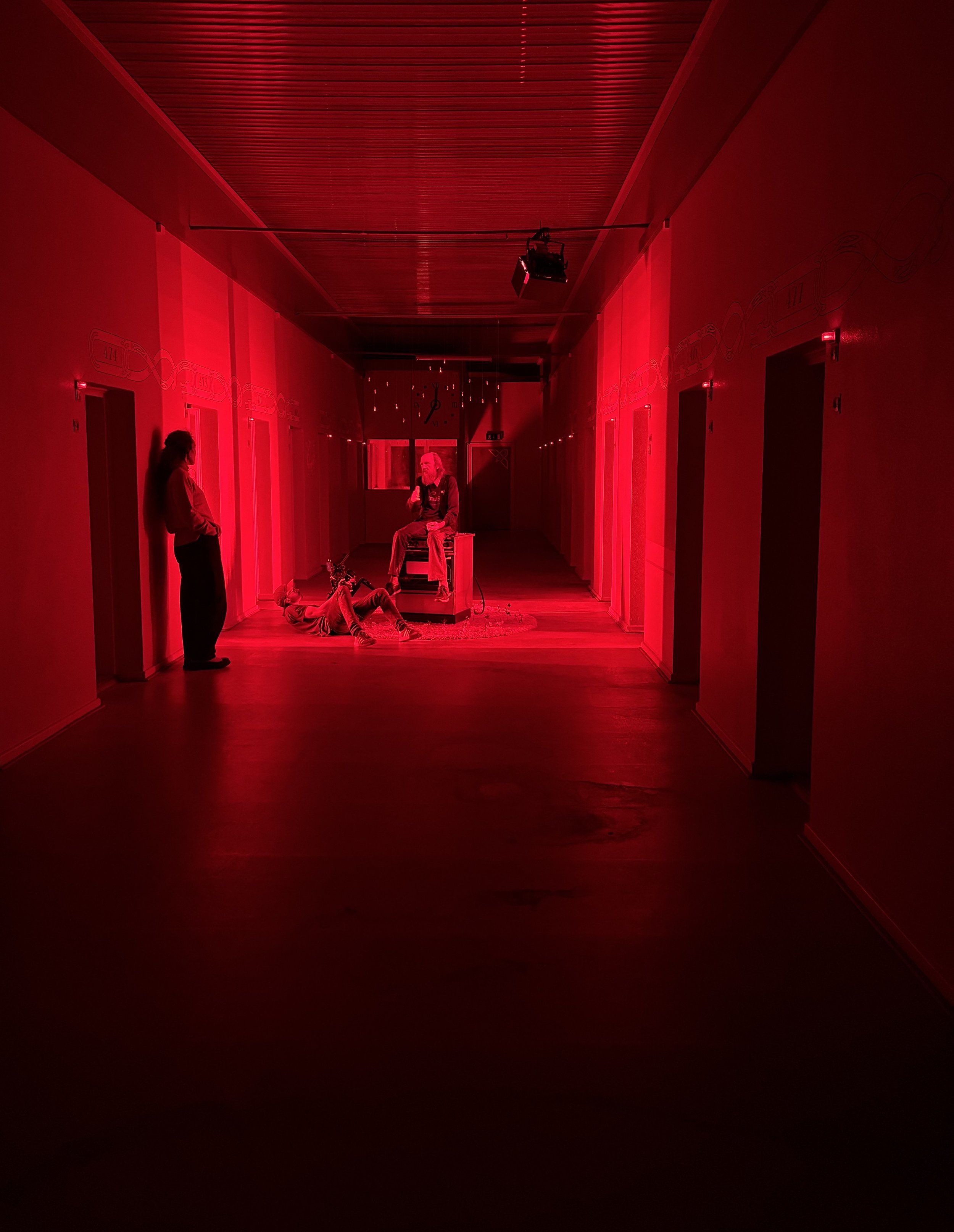 	
En mørk korridor med rødt lys, hvor en person sidder på en gammel gasovn. Der er filmudstyr, herunder et kamera, rettet mod personen på scenen. | Dokumentarfilm | Retrograd | Esben Persson & Anders Mielcke | Filmproduktion Aarhus | GESTALT