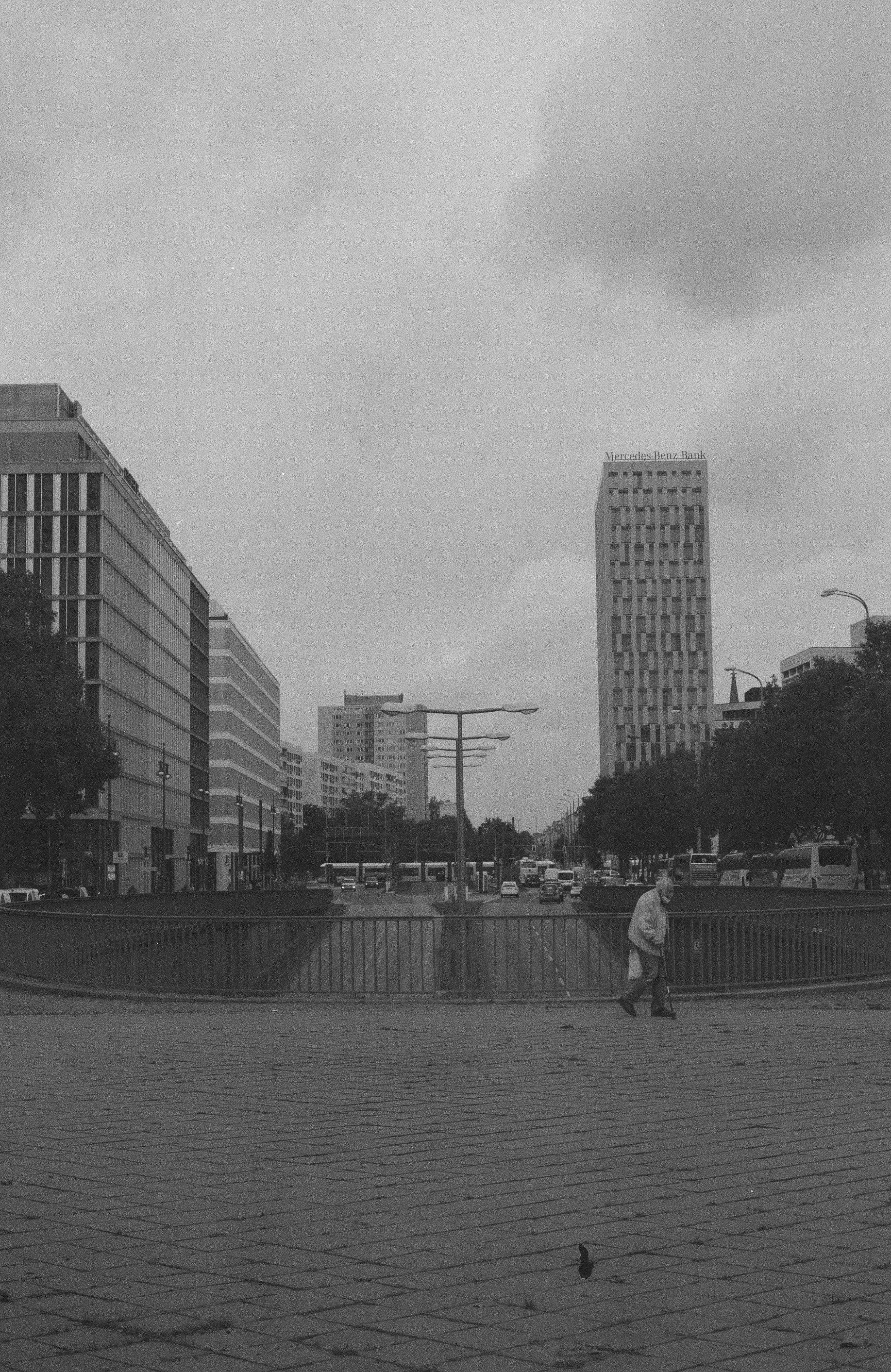 Sort-hvid bybillede af en gade med høje bygninger, busser og biler, og en ældre person, der går forbi med en stok | Location scouting | Kodak | Analoge optagelser | Filmproduktion Aarhus | GESTALT