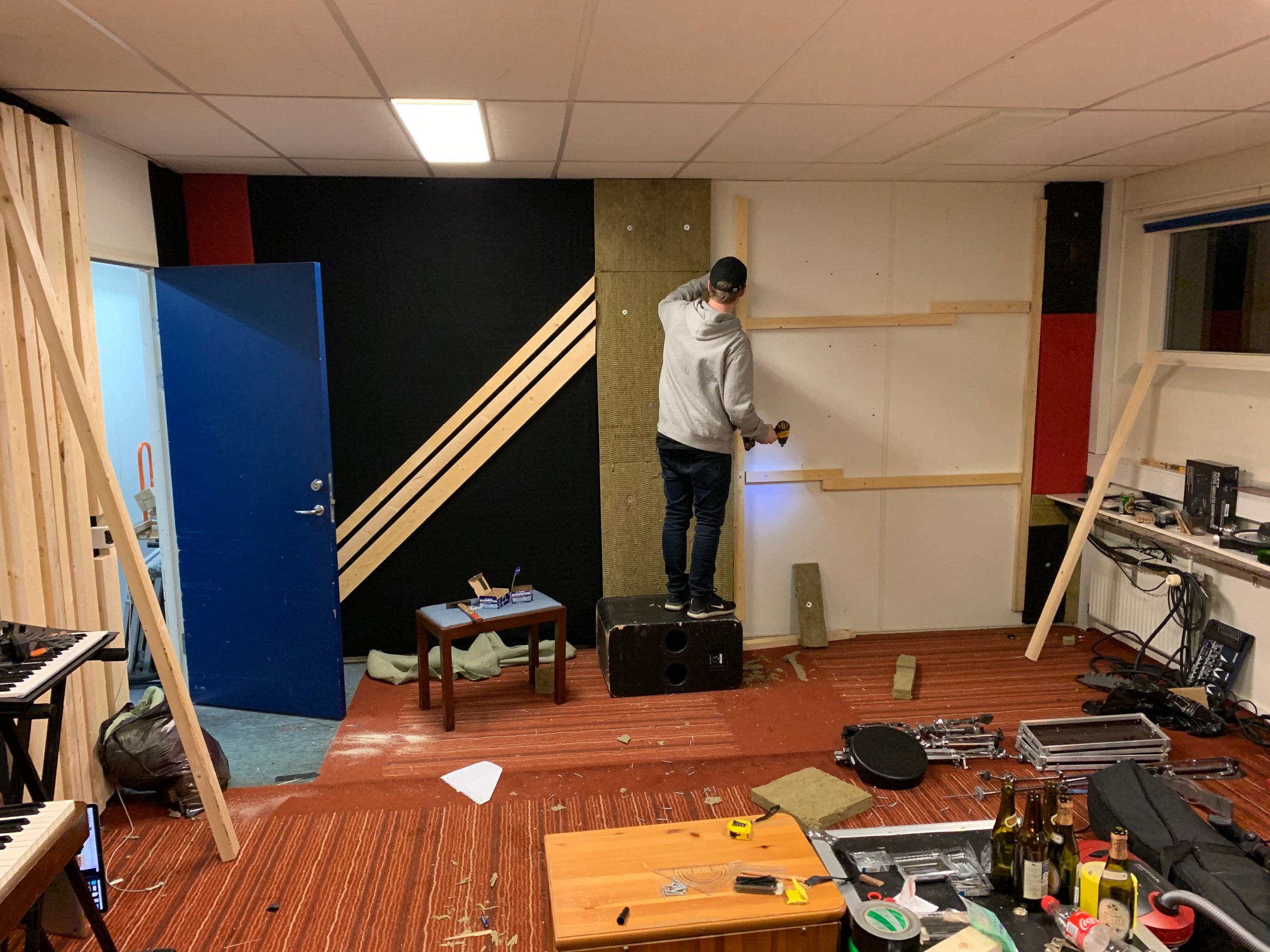 En person arbejder på at opbygge en væg i et værelse med værktøj og materialer spredt ud over gulvet | Musikkomposition | Studieproduktion og lyddesign | Filmproduktion Aarhus | GESTALT