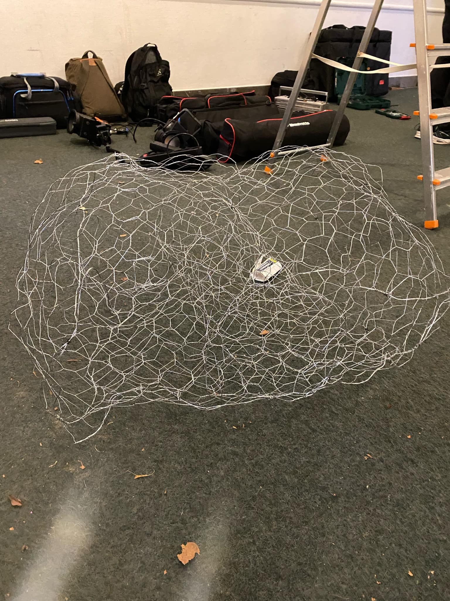 Et metalnet på gulvet i et rum med forskellige tasker og udstyr i baggrunden | Dokumentarfilm | Retrograd | Esben Persson & Anders Mielcke | Filmproduktion Aarhus | GESTALT