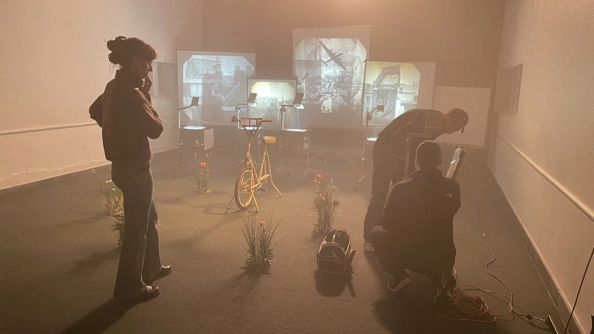 Tre personer i et rum med kunstprojektioner, en cykel, blomster og computerskærme | Dokumentarfilm | Retrograd | Esben Persson & Anders Mielcke  | Filmproduktion Aarhus | GESTALT