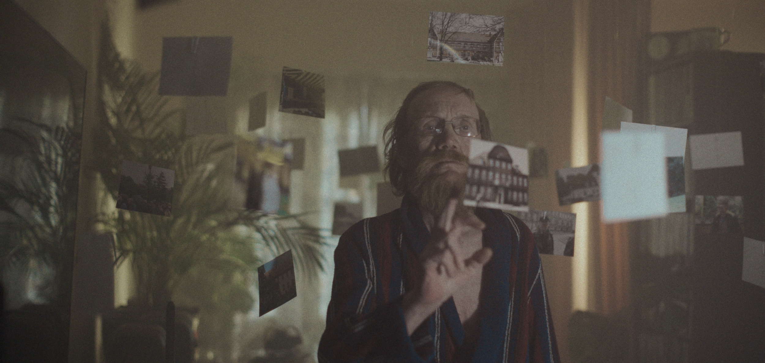 En mand med skæg og briller betragter fotografier, der svæver i luften i et mørkt rum | Dokumentarfilm | Retrograd | Esben Persson & Anders Mielcke | Filmproduktion Aarhus | GESTALT