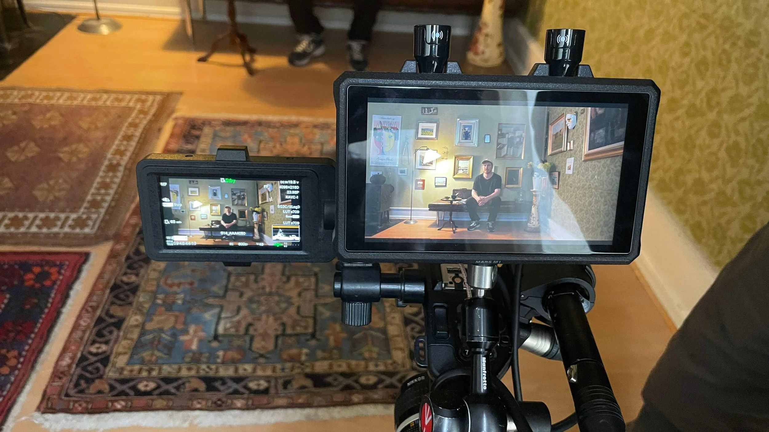 Et video kamera med monitor der viser en person sidende på en sofa i en stue med vægdekorationer | Dokumentarfilm | Retrograd | Esben Persson & Anders Mielcke | Filmproduktion Aarhus | GESTALT