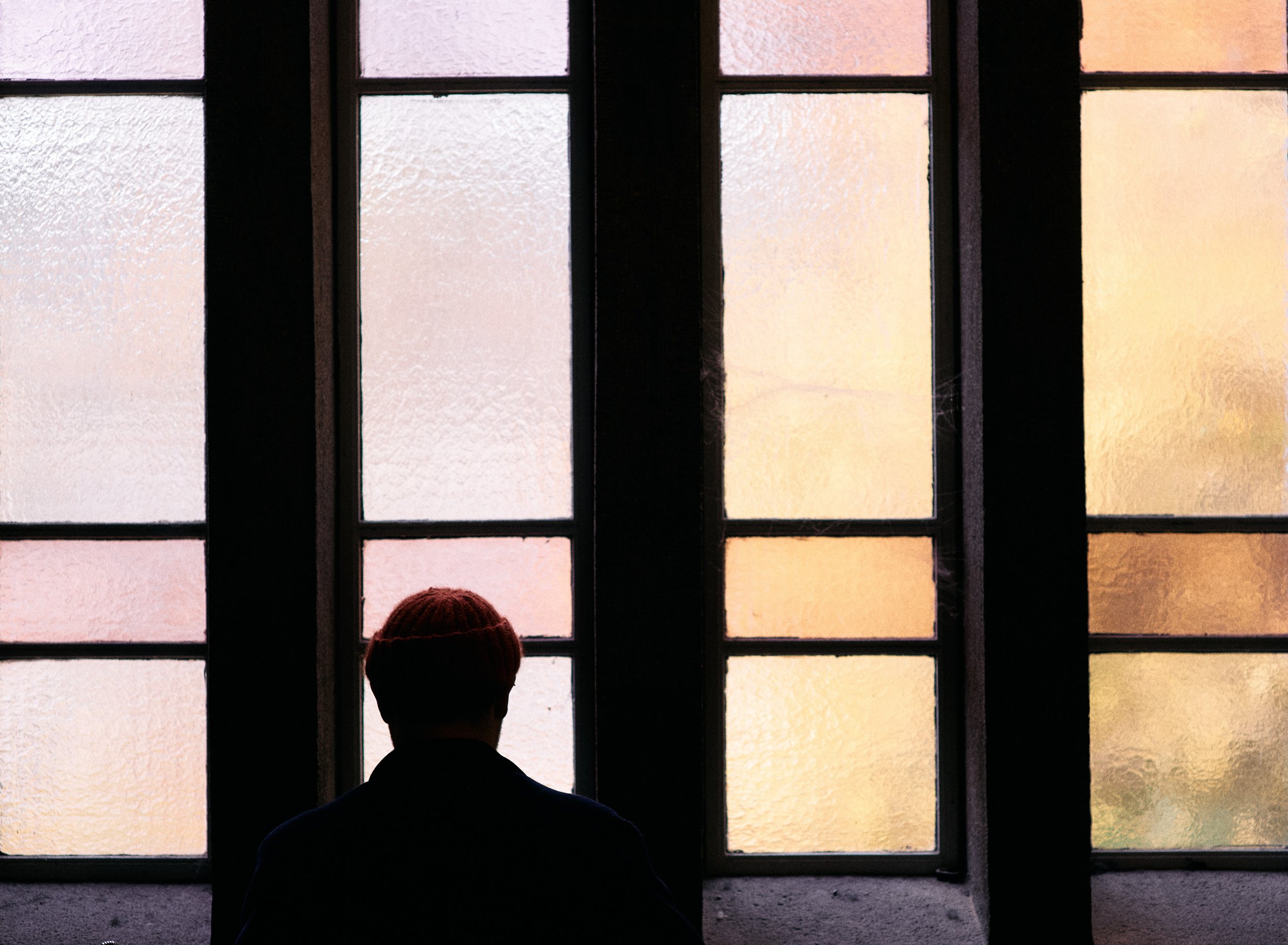 Person sidder foran et farvet vindue i et mørkt rum | Dokumentarfilm | Retrograd | Esben Persson & Anders Mielcke | Filmproduktion Aarhus | GESTALT