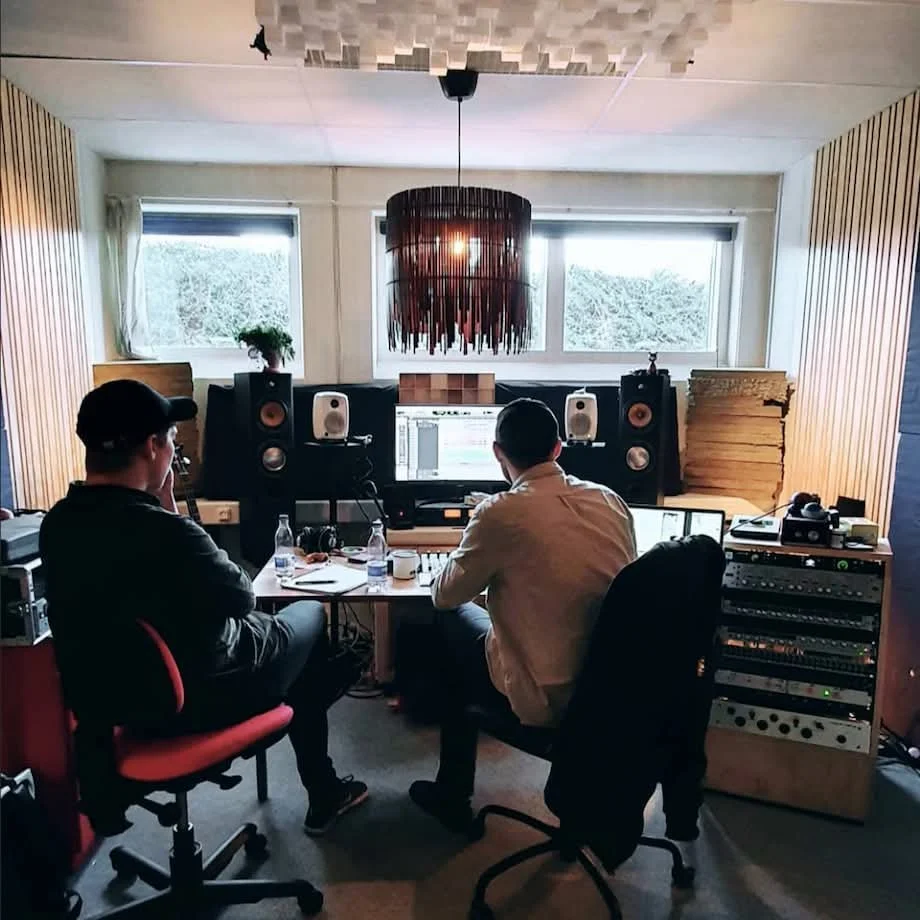 To personer arbejder i et musik- eller lydstudie med professionelle højtalere, computer og lydudstyr | Musikkomposition | Studieproduktion og lyddesign | Filmproduktion Aarhus | GESTALT