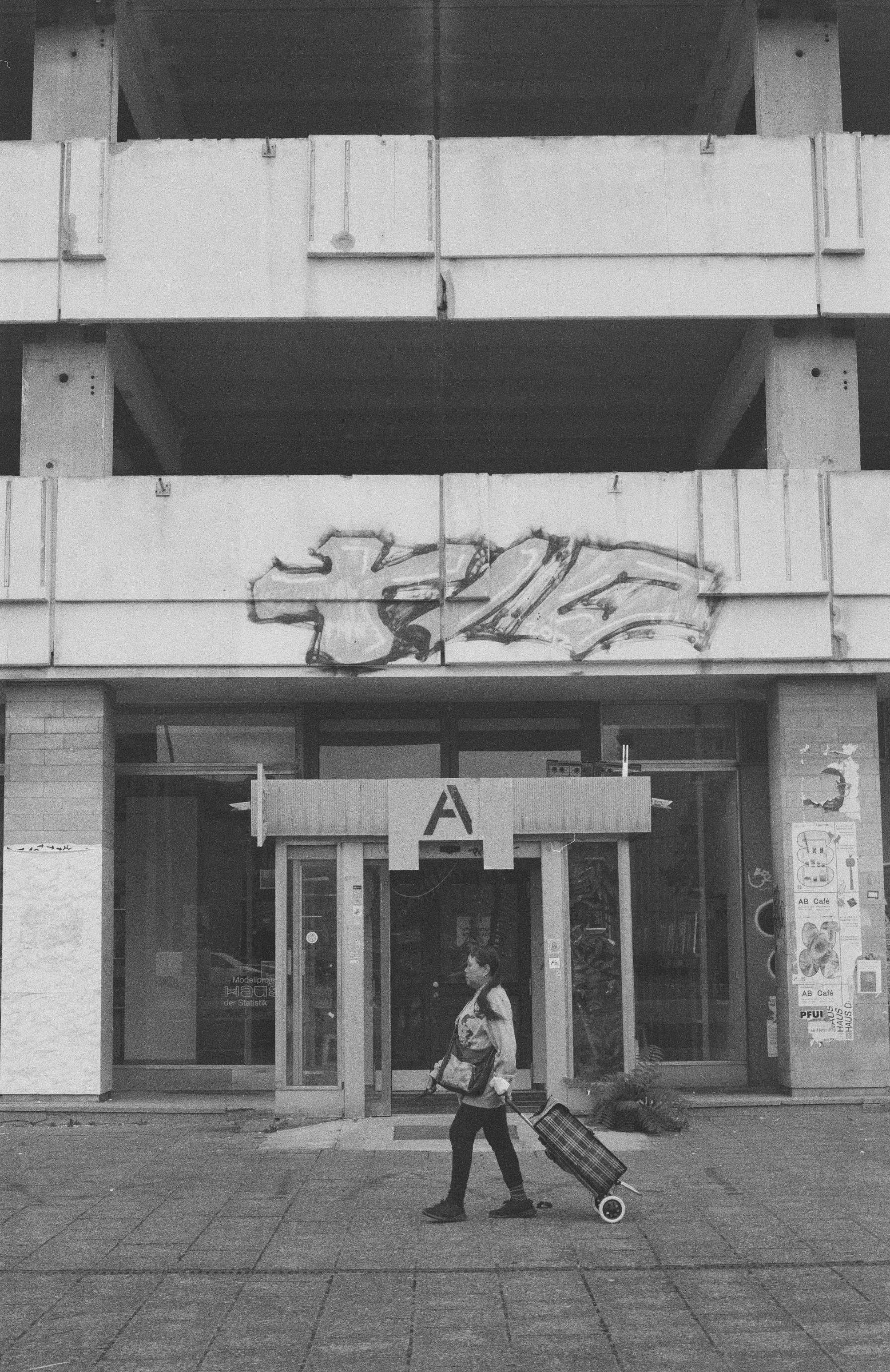 En person går foran indgangen til en bygning med en rejsetaske, på en grå dag | Location scouting | Kodak | Filmproduktion Aarhus | GESTALT