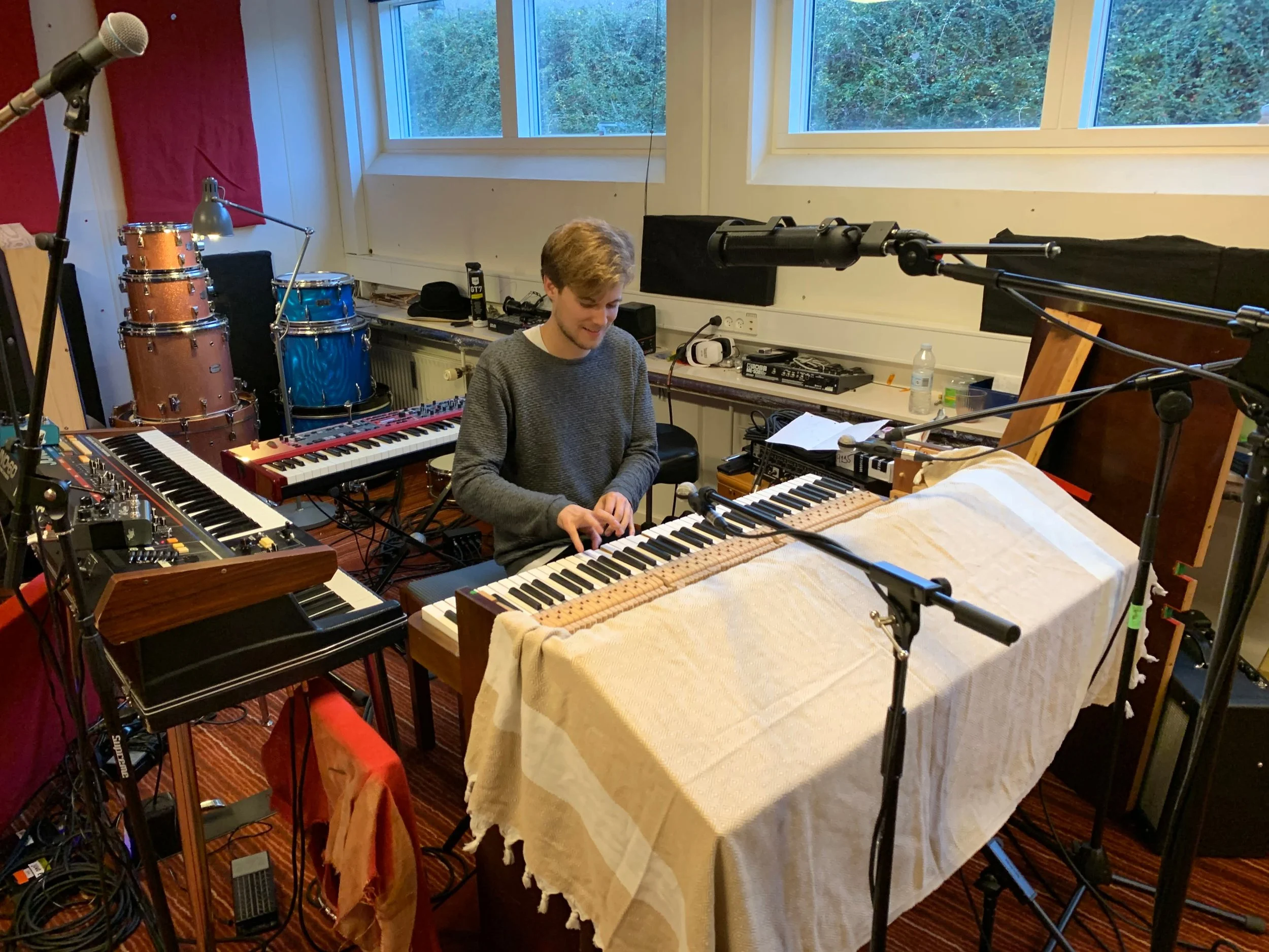 En mand spiller på et keyboard i et musikstudie, omgivet af forskellige musikinstrumenter og mikrofoner | Studieproduktion | Musikkomposition | Filmproduktion Aarhus | GESTALT