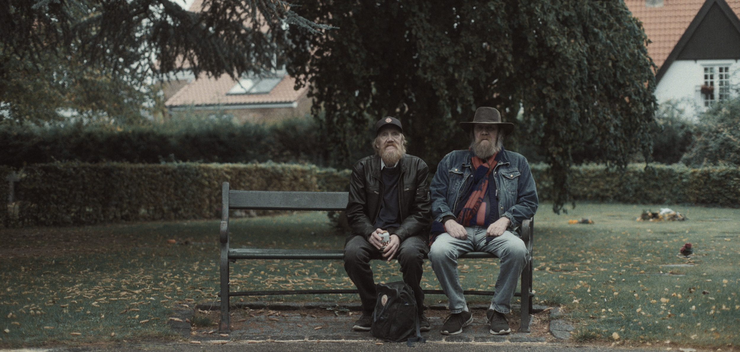 To ældre mænd sidder på en parkbænk under et træ, én holder en øl, og der ligger en rygsæk foran dem | Dokumentarfilm | Retrograd | Esben Persson & Anders Mielcke | Filmproduktion Aarhus | GESTALT