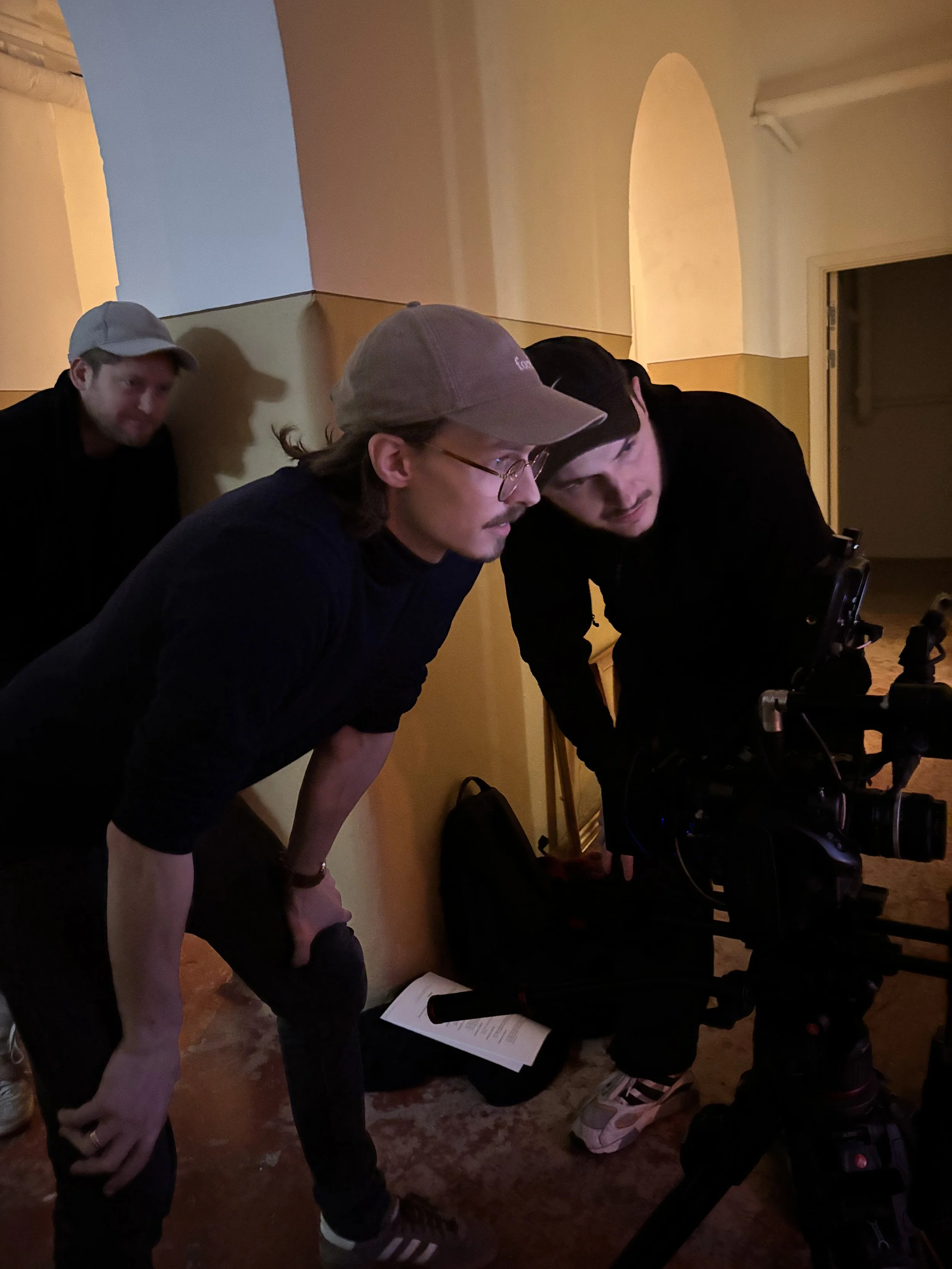 Tre personer står tæt sammen, og kigger på et filmkamera, i et scenisk indendørs miljø | Dokumentarfilm | Retrograd | Esben Persson & Anders Mielcke | Filmproduktion Aarhus | GESTALT